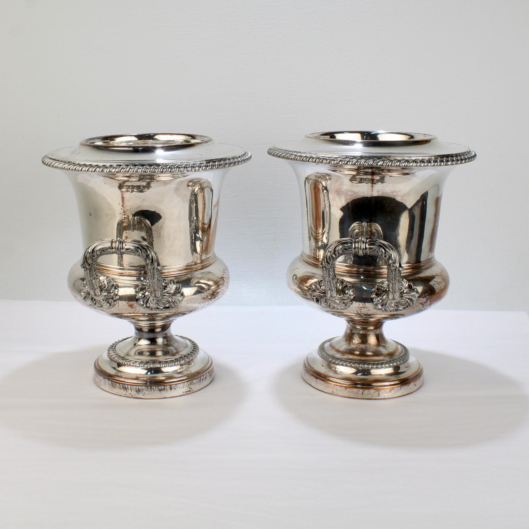 A fine pair of antique English wine coolers. 

Each wine cooler is plated with silver on copper, has a gadrooned top rim, tops and liners that seat fairly well, ornate twin handles, and a stepped trumpet-form base. 

Both have had a crest or