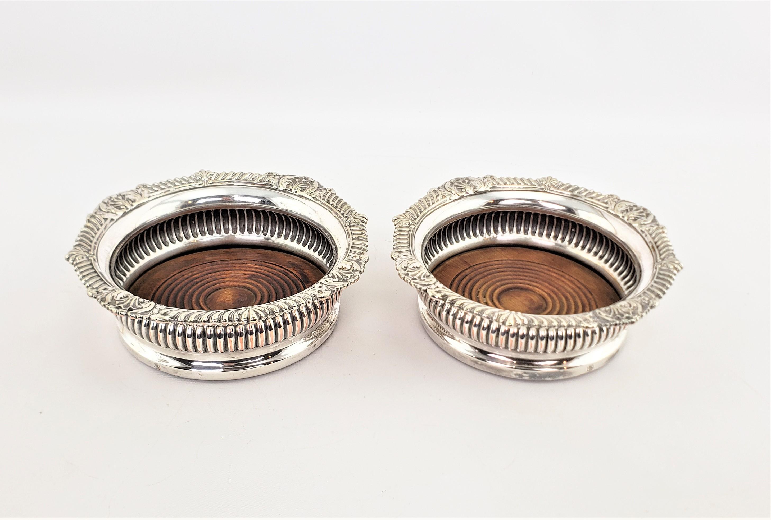 This pair of large wine bottle coasters are unsigned with respect to the maker, but originate from England and date to approximately 1920 and done in a Victorian style. The bottle coasters are composed of silver plate with deep ribbed sides and a