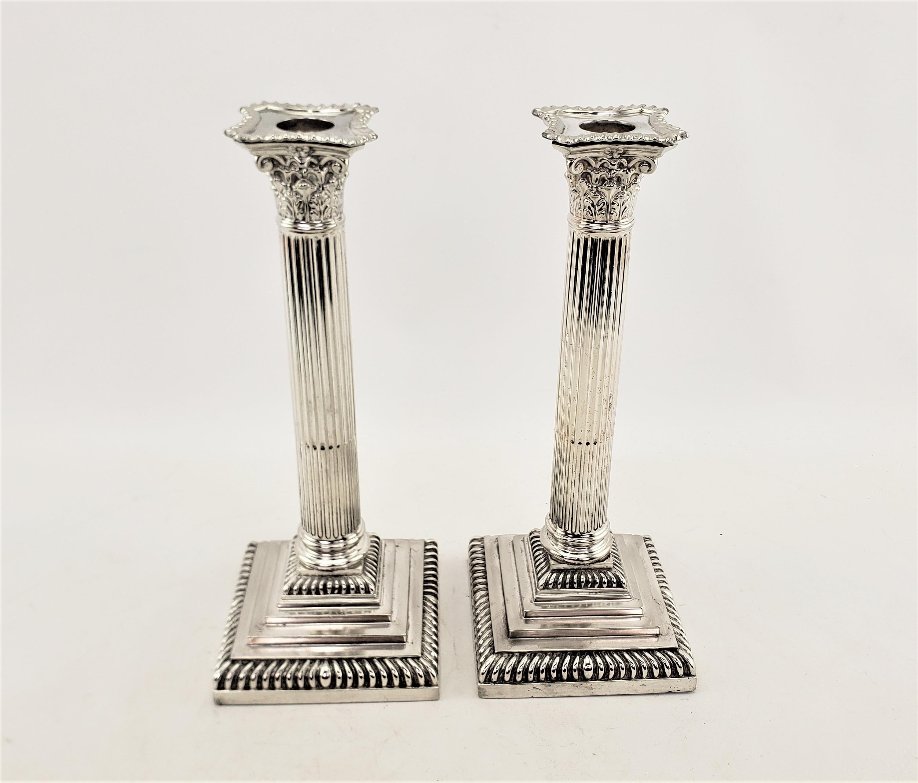 This pair of antique candlesticks are hallmarked by an unknown maker, and presumed to originate from England and date to approximately 1920 and done in a Greek Revival style. The candlesticks are composed of silver plate and are done as Corinthian