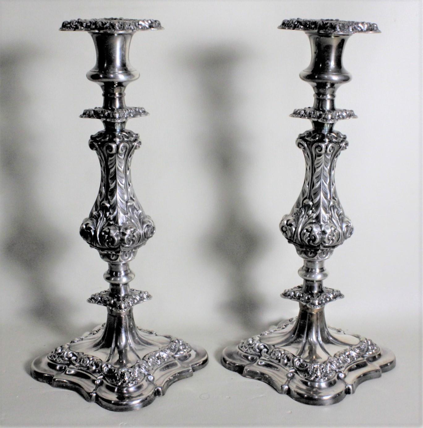 This pair of antique silver plated candlesticks were made in England, likely by Ellis & Barker, in circa 1900 in the period Edwardian style. The candlesticks are heavily chased with a stylized leaf decorative motif from the cups to the bases. Each