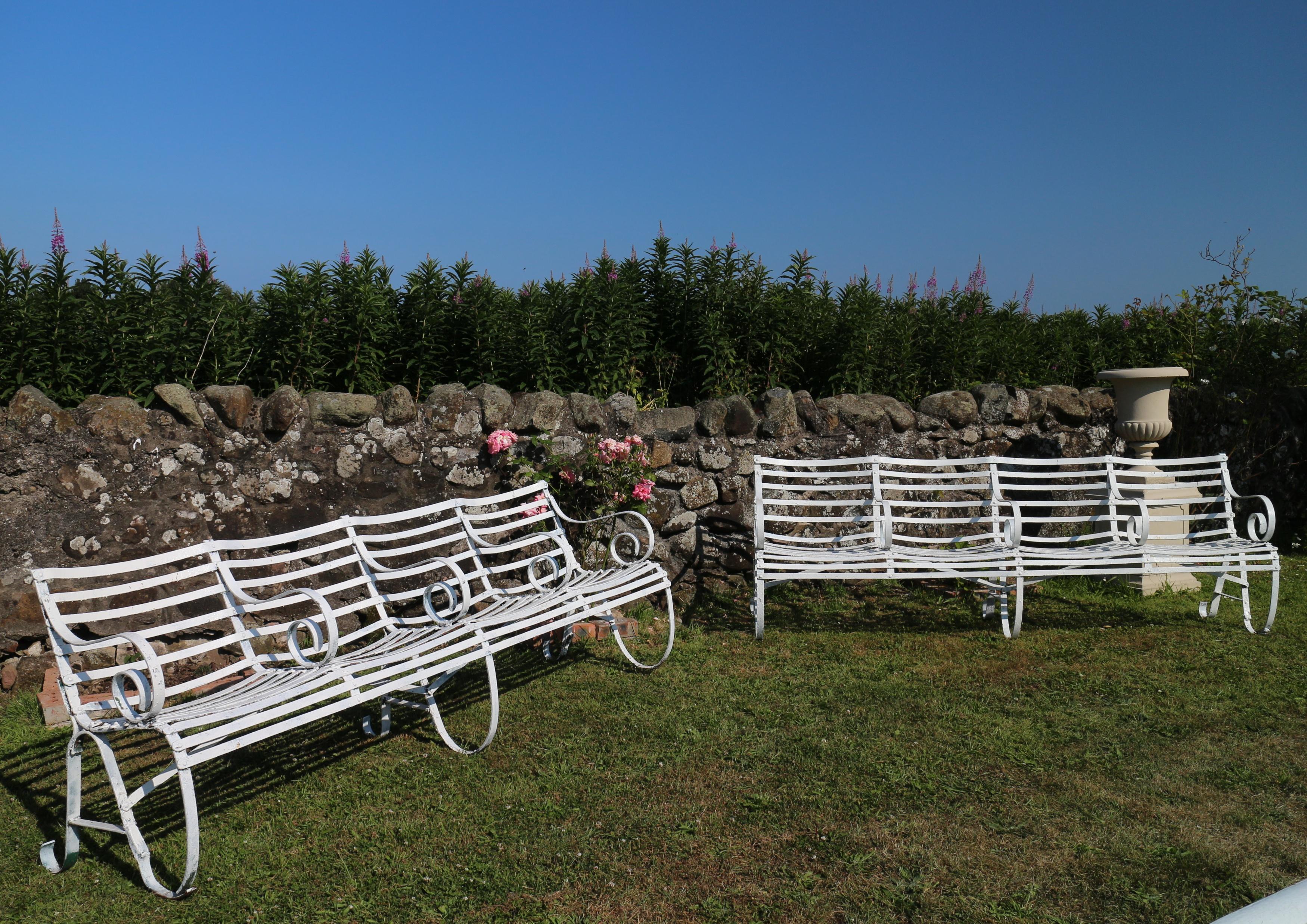 A pair of unusual 19th century wrought iron garden seats or benches, with ornate scrolling armrests and ergonomically curved back and seats for each place. With scrolling legs to the middle and ends and braces between the legs for plenty of support.