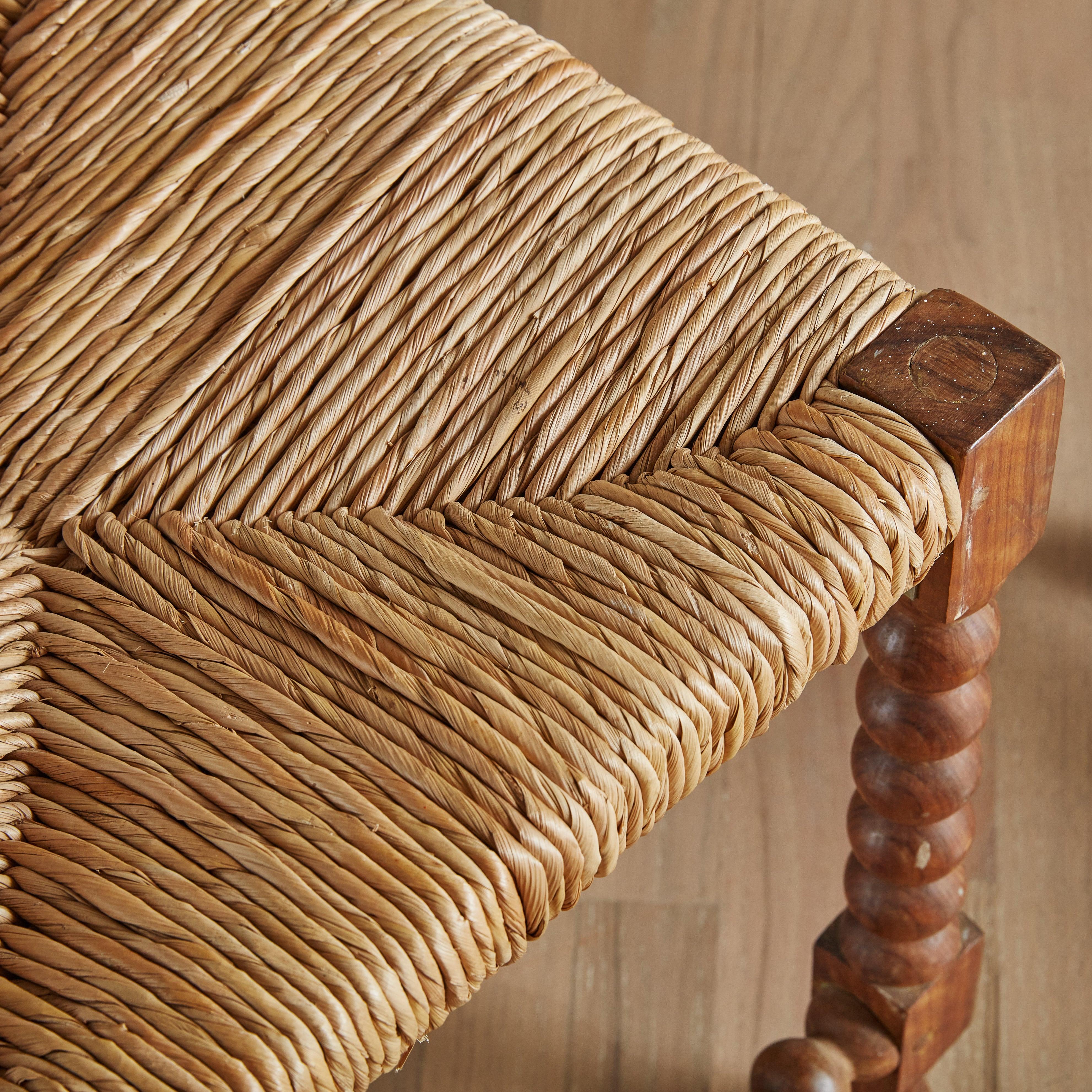 A pair of antique English style low stools featuring square woven rush seats and patinated walnut frames. Each stool is raised on four bobbin legs connected to one another by a single side stretcher. These stools function as seating, though we also
