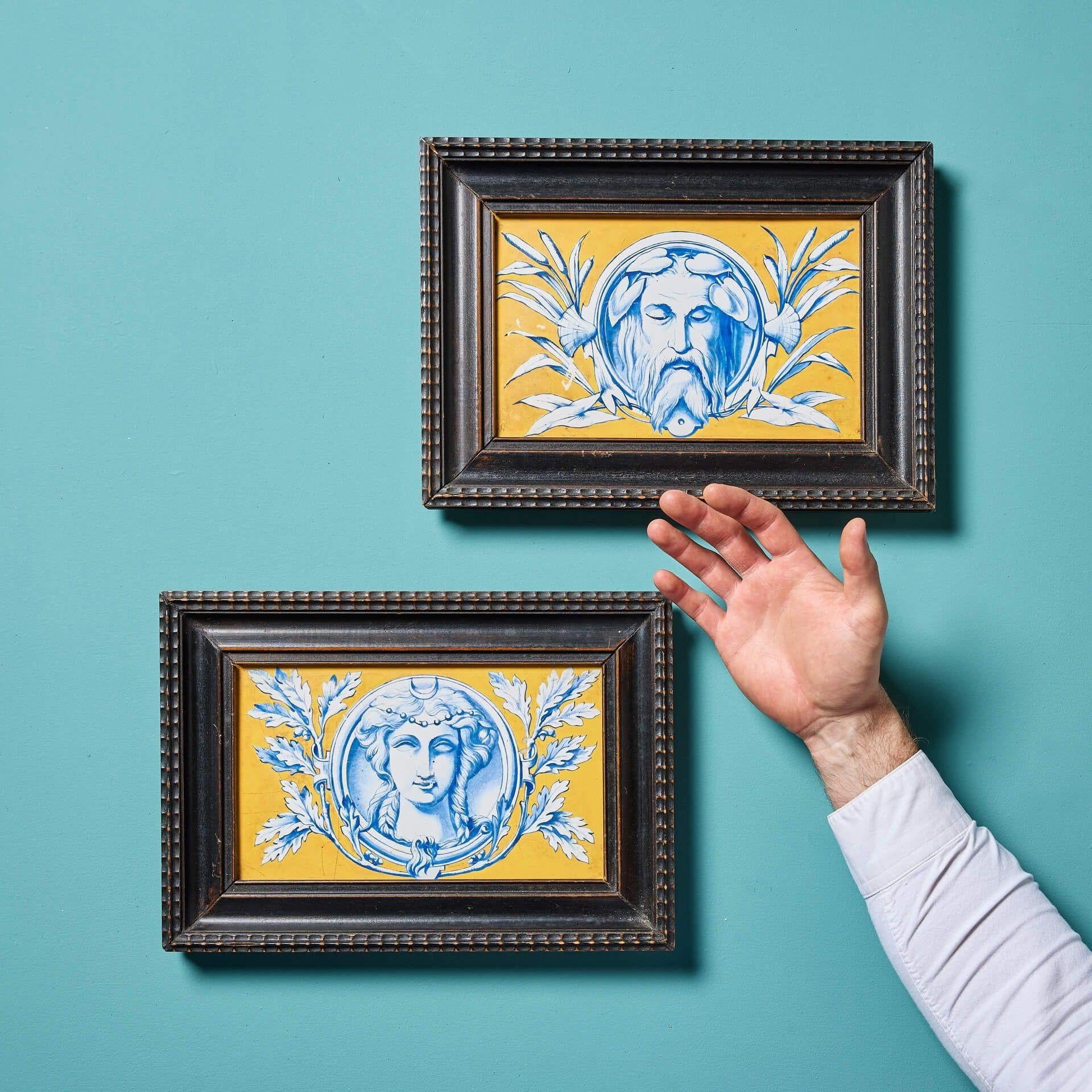A pair of antique framed tile panels depicting decorative Neoclassical portraits.

Dating to circa 1870, each plaque is carefully hand painted in a tonal blue on a vivid ochre background.

The woman is displayed with a crescent moon to represent the