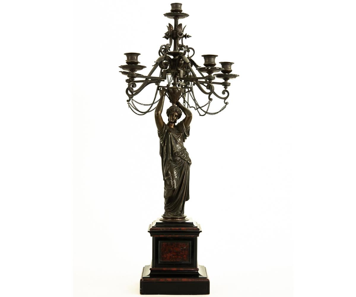 Offered is this fine pair of bronze six-light candelabras, each with a classical female figure in flowing drapery holding aloft a classical urn, from which are protruding decorative arms, draped with chains, which ultimately support the candles. The