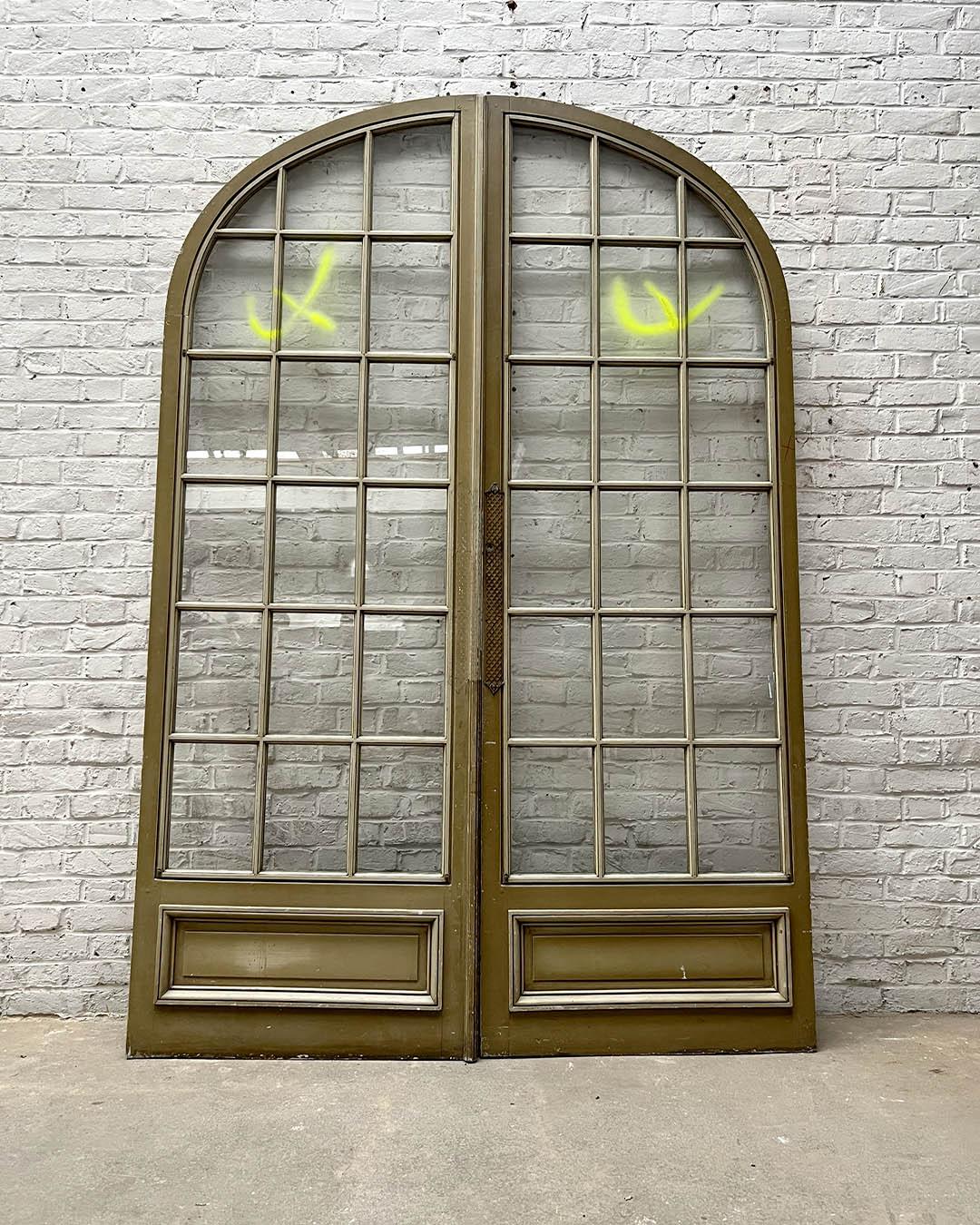 Elegant pair of French double doors with arched tops, dating from the early 20th century. Crafted in painted wood with multiple glazed panels and molded lower sections, they feature refined decorative metalwork around the lock strip.

The original