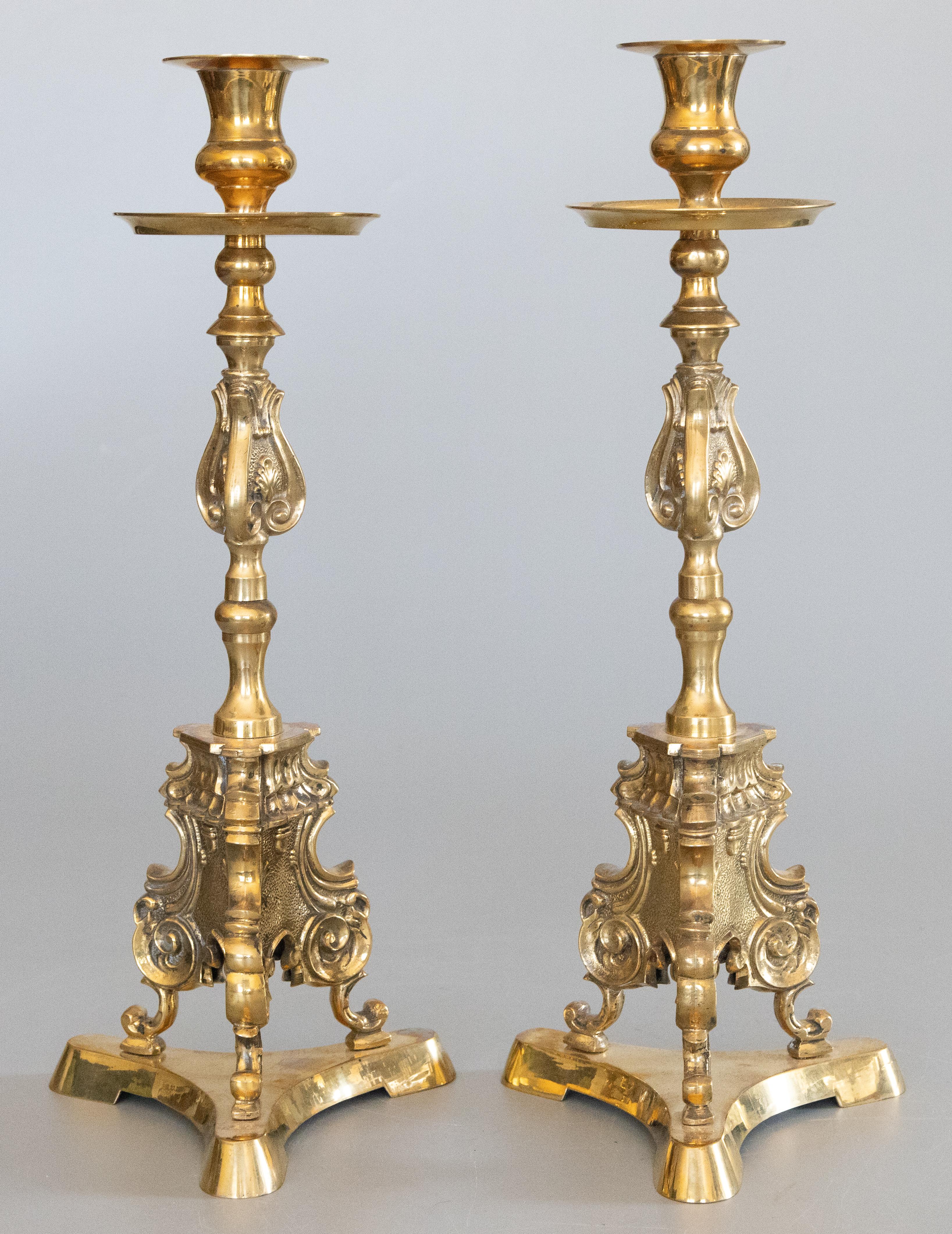 A superb pair of antique French brass altar candlesticks with a triangular base, circa 1920. These fine cathedral candlesticks are decorated with stylized acanthus leave and handsome scrollwork with a lovely brass patina. They display beautifully,