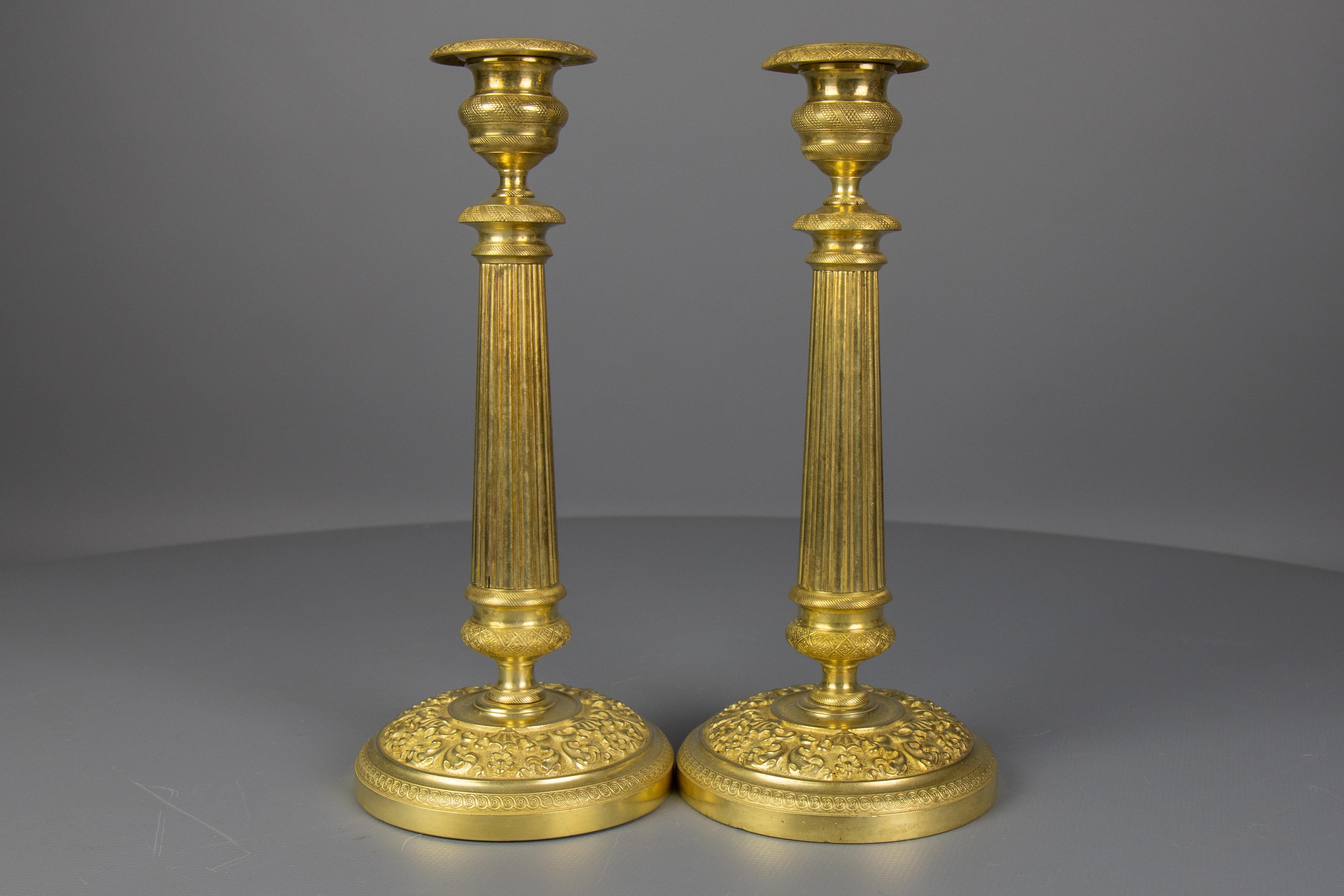 Una bella coppia di antichi candelieri in ottone in stile Restauration francese con bobeches (vassoi di raccolta) rimovibili, risalenti al 1920 circa. Ogni candeliere è caratterizzato da uno stelo colonnare scanalato, ha un collare ornato, decorato