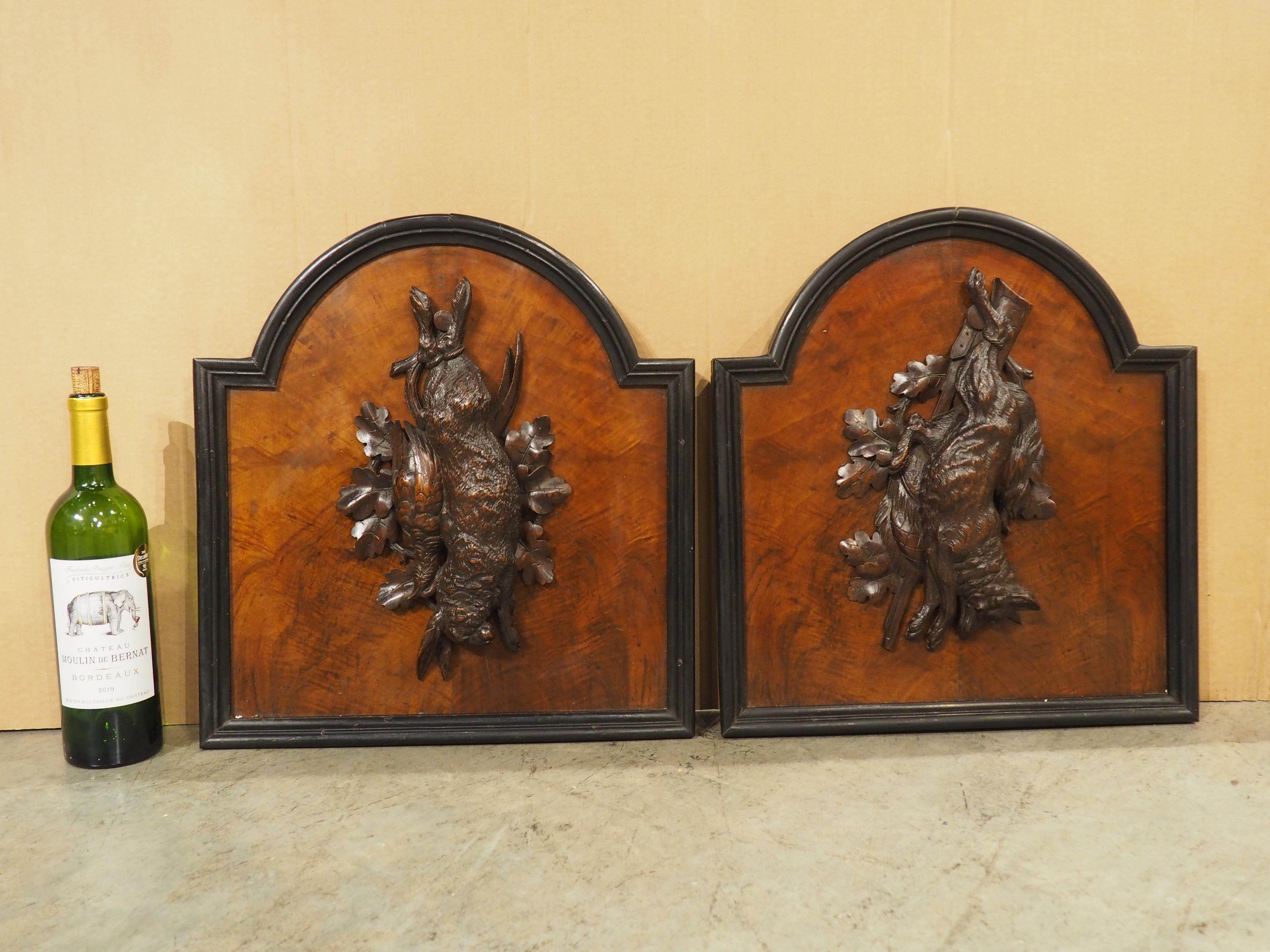 Hand-carved in France during the early 1900s, this pair of hunt plaques feature raised game carvings on each panel, backed by luxurious reddish-brown burlwood with intense graining. Both plaques are rectilinear with an arched top, surrounded by