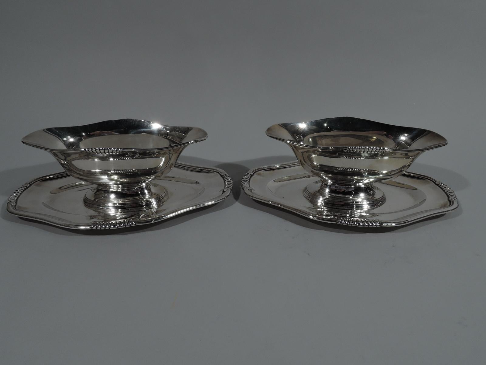 Pair of French 950 silver Classical gravy boats on stands, circa 1910. Each: Boat has tapering ends, curved and tapering bowl, and stepped oval foot mounted to shaped stand with oval well. Scrolled and gadrooned rims. Single letter monogram engraved