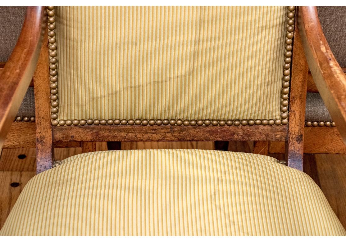 Coppia di poltrone in stile Impero in radica di noce con sedili e schienali imbottiti, caratterizzate da un'accurata lavorazione artigianale con una barra superiore quadrata e un accento intagliato stilizzato sulla parte anteriore di ciascun