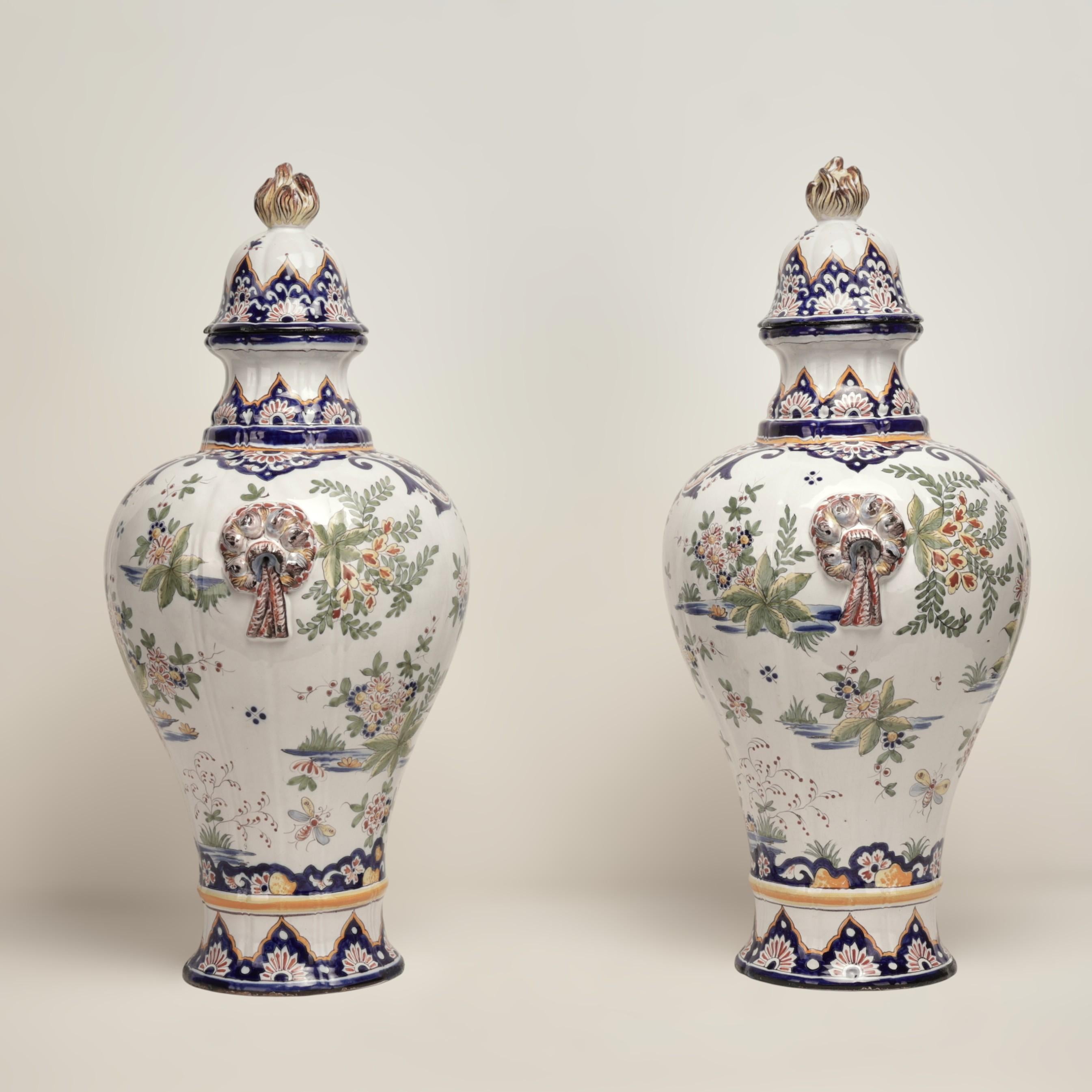 Standout pair of large 19th century French faience earthenware lidded urns handcrafted in classic form featuring tassel form handles, flame finials and hand decorated floral designs all around.