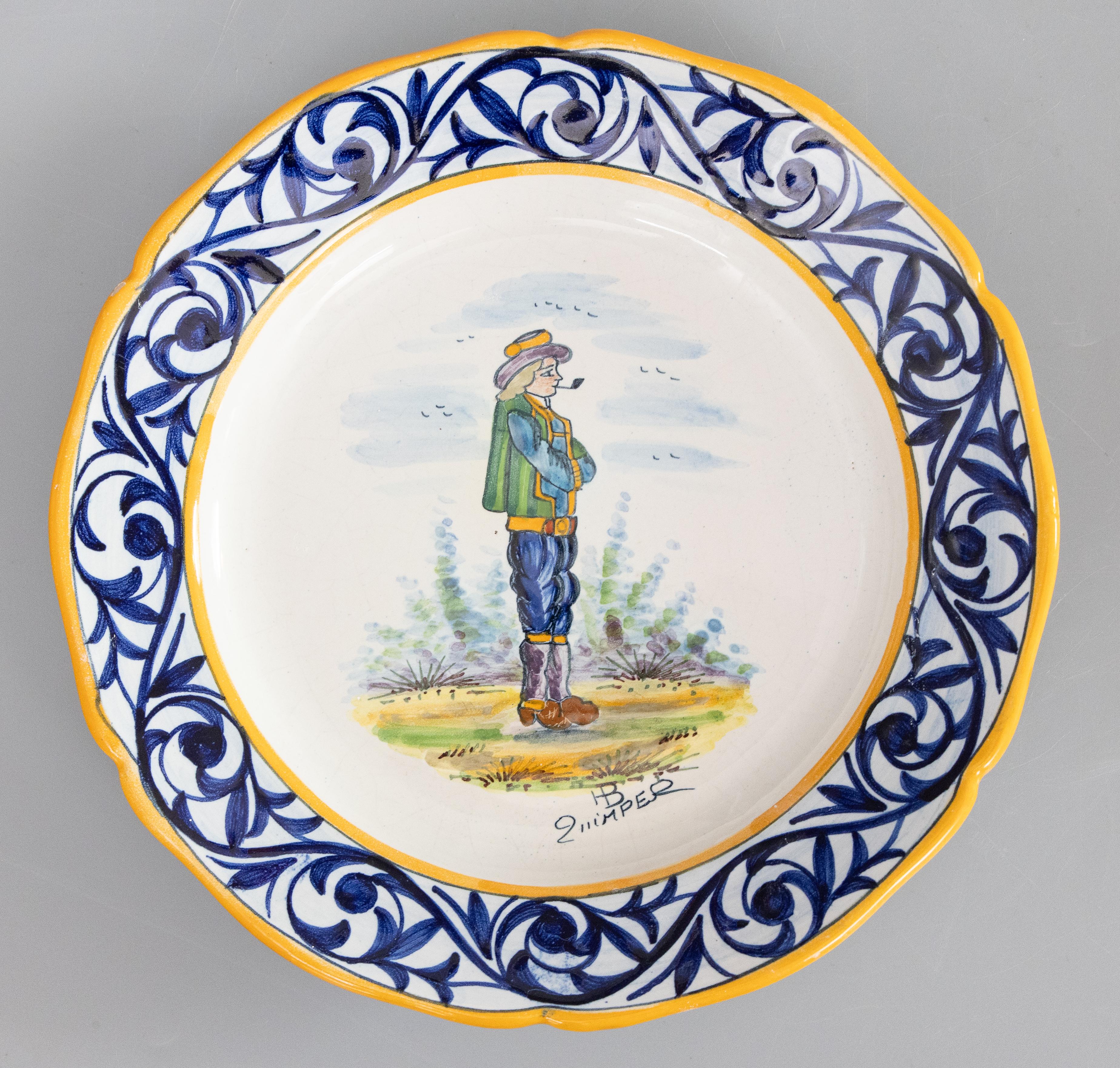 Une charmante paire d'assiettes anciennes en faïence de Quimper, vers 1920. Marque du fabricant au recto et au verso. Ces assiettes de collection peintes à la main représentent l'homme breton fumant la pipe et la femme bretonne tricotant, avec une