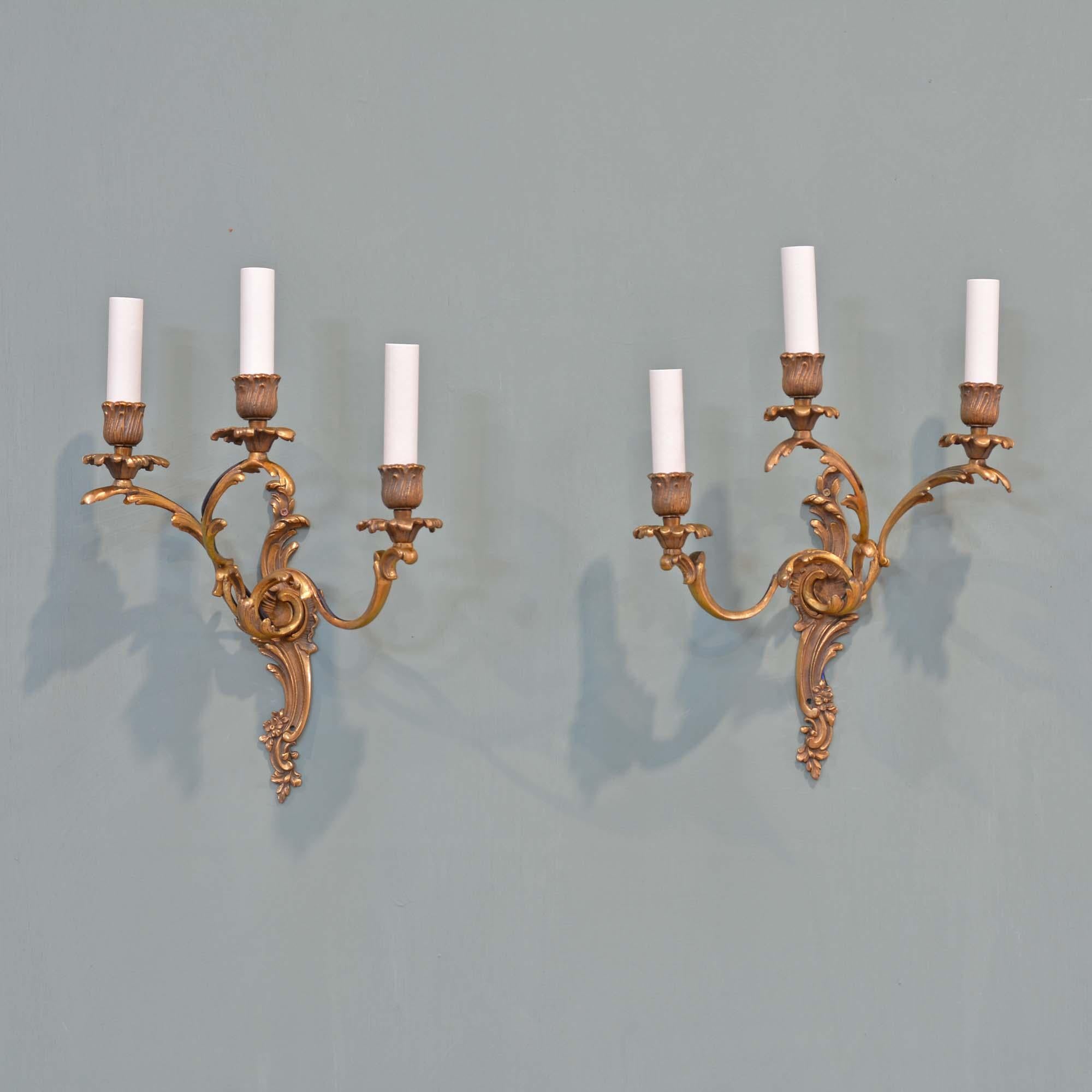 Pair of gilt brass Rococo wall lights
Gilt brass three arm lights in the Rococo style, a mirrored pair with S-scroll foliate wall plates, bobeche and candle holders.
French, circa 1930

Rewired and fitted with new candle tubes. To take E14 - Small