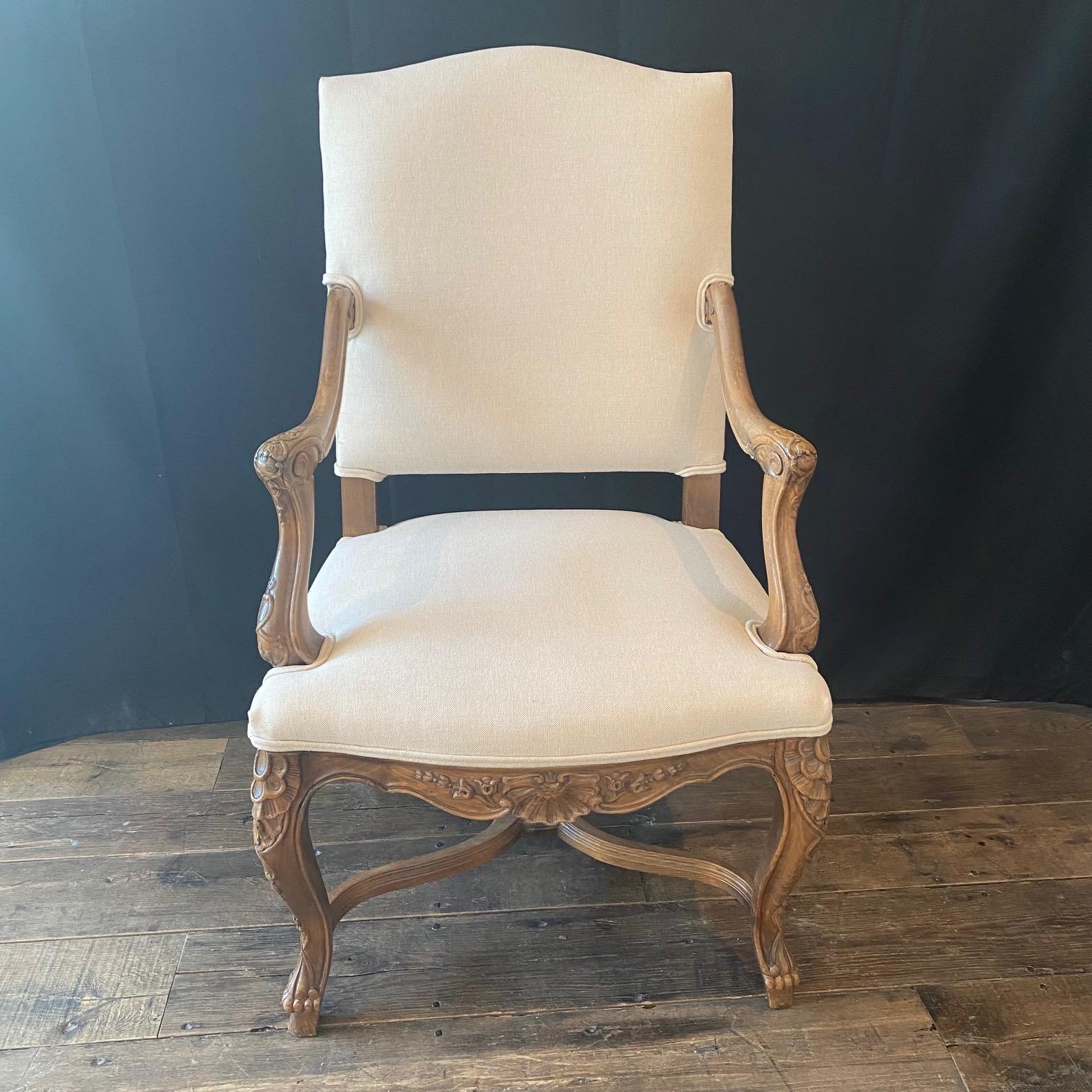Lovely pair of carved antique French Louis XV armchairs with new neutral British upholstery sculpted from fine walnut featuring exquisitely formed frameworks with subtly arched seatback crowns, gracefully scrolled armrests, and undulating aprons