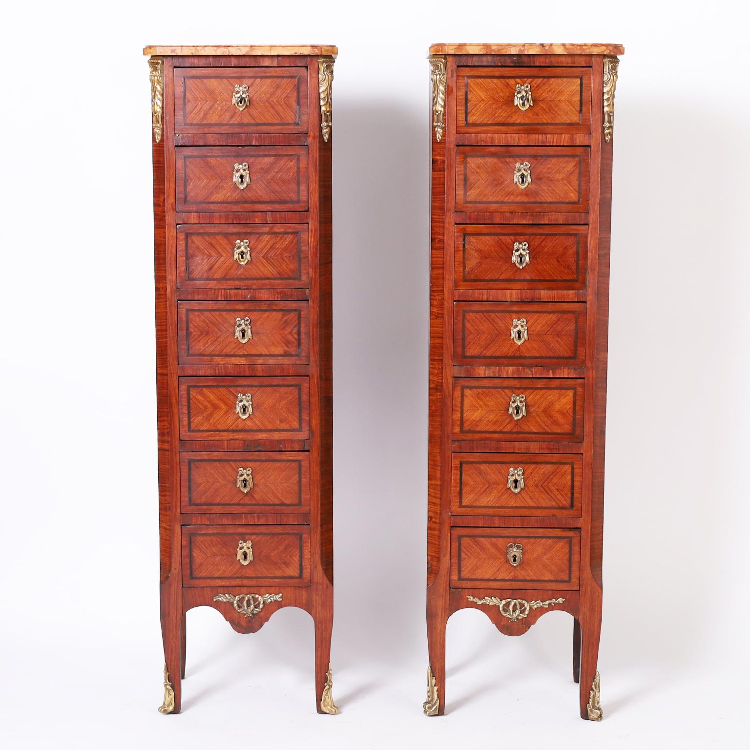Refined pair of 19th century French lingerie chests with marble tops on seven drawer cases crafted in tulipwood and walnut decorated with gilt bronze ormolu, drapery escutcheons, and floral wreaths.