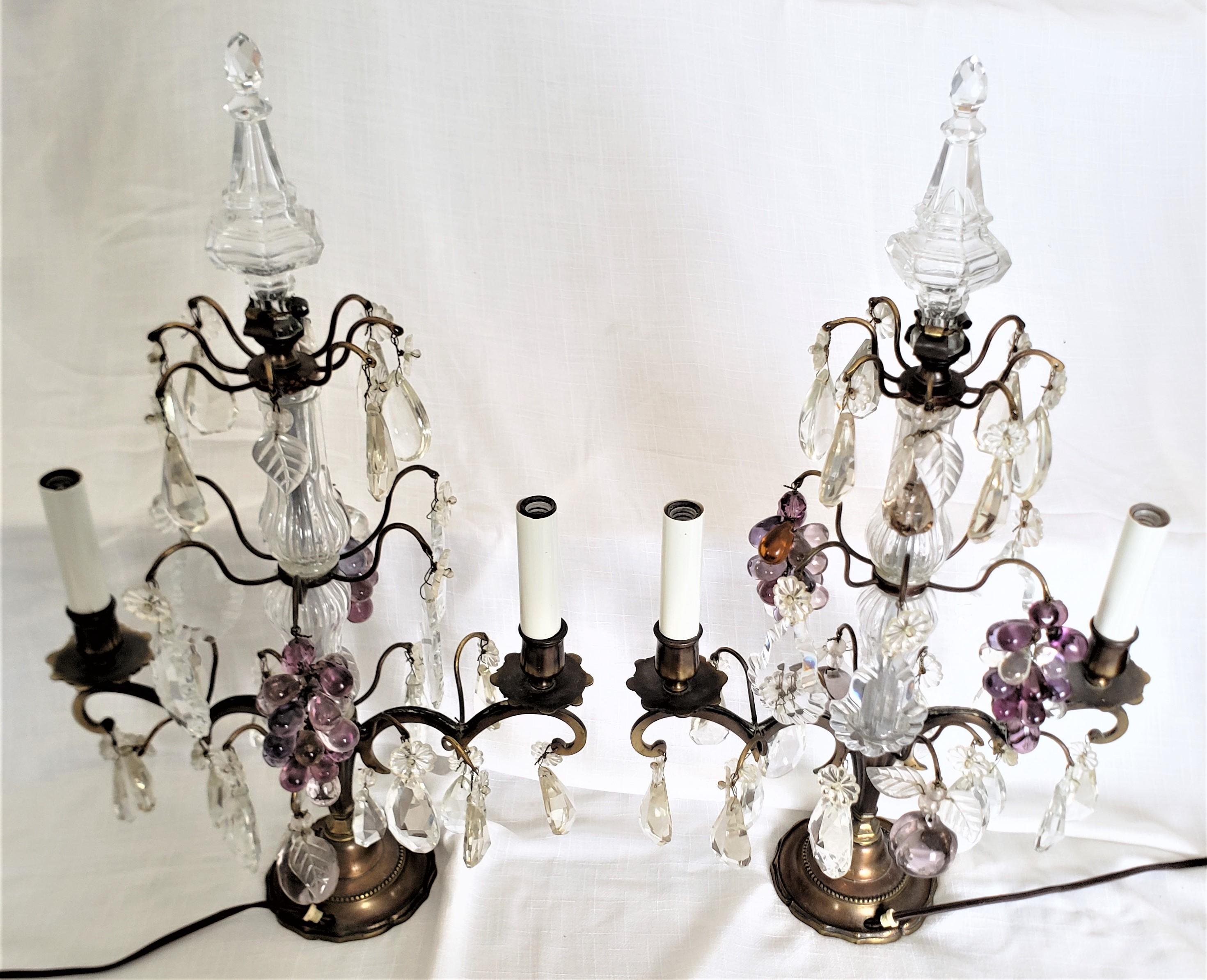 This pair of antique brass and crystal lamps are unsigned, but presumed to have originated from France and date to approximately 1900 and done in a Louis XV style. Each lamp is done with a solid brass frame with two candelabra styled lights and