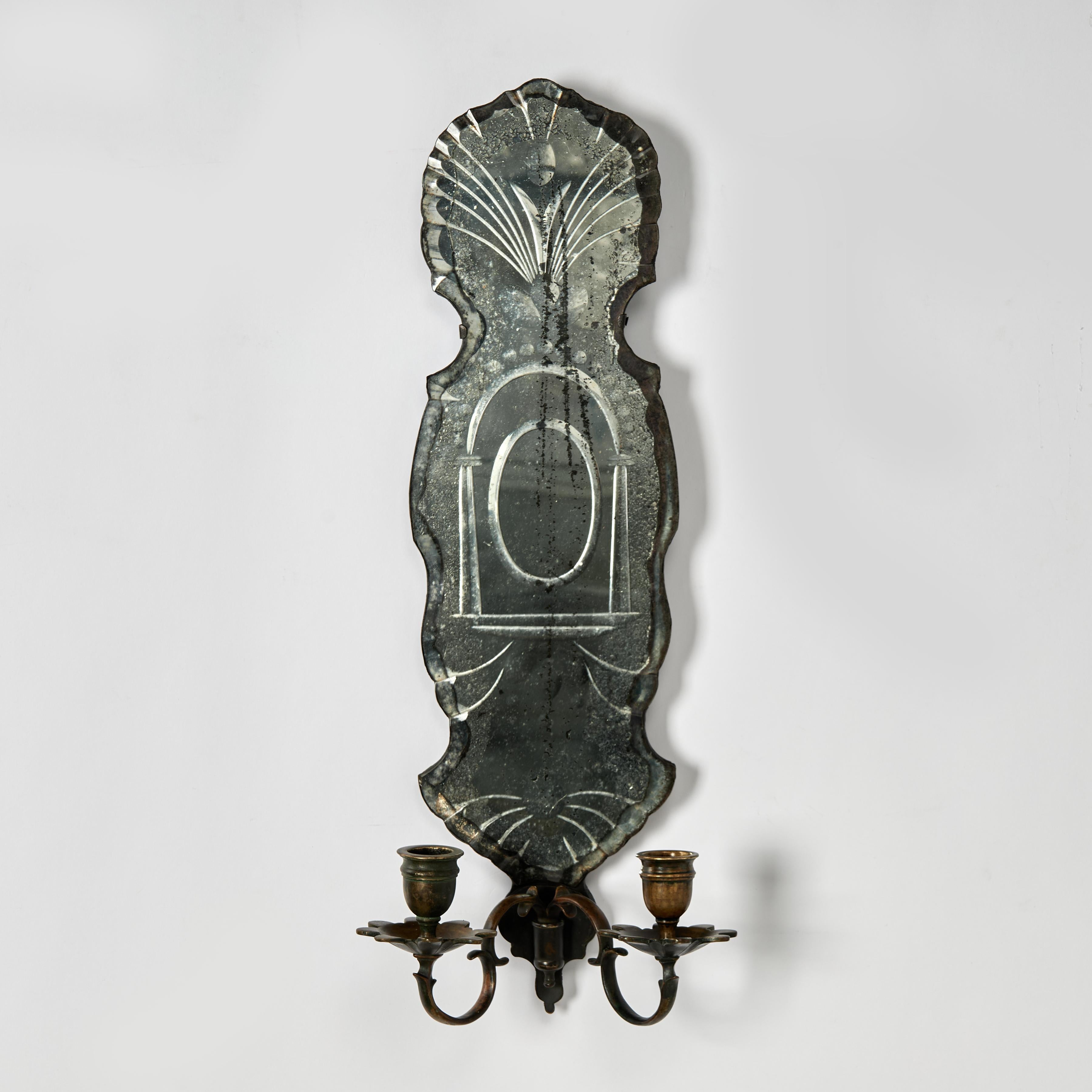 Impressive pair of neoclassical 19th century French wall sconces crafted with a beveled mirrored backplate with reverse etched architectural designs and a perfectly aged oxidized finish, over two elegant brass arms, bobeches and candle cups with a