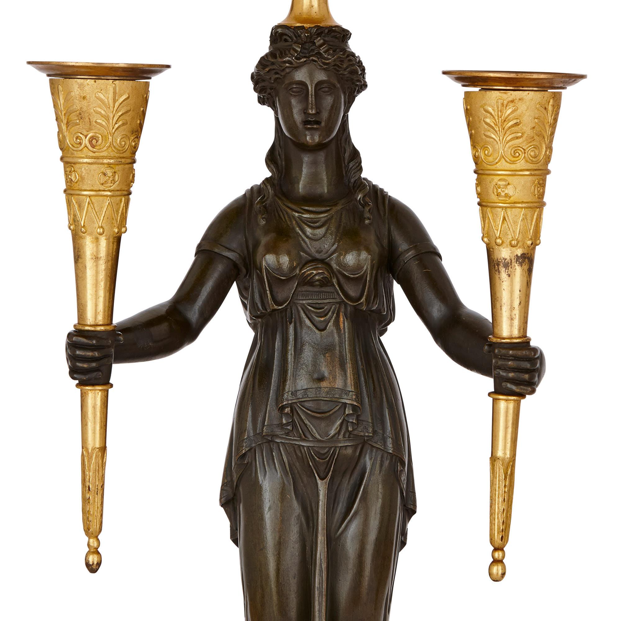 These bronze candelabra were created in France in circa 1810, when Napoleon Bonaparte was Emperor. The candelabra combine neoclassical and ancient Egyptian motifs, in a manner characteristic of Empire period decorative art. 

The candelabra have