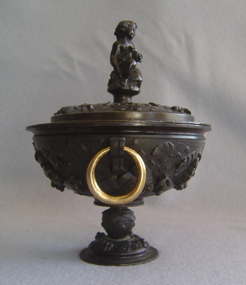 An attractive pair of French patinated bronze lidded urns. Set on a round socle the body of the urns are decorated with leaves and berries. To each side is a circular, gilt ring handle. The lids are similarly decorated with leaves and berries and