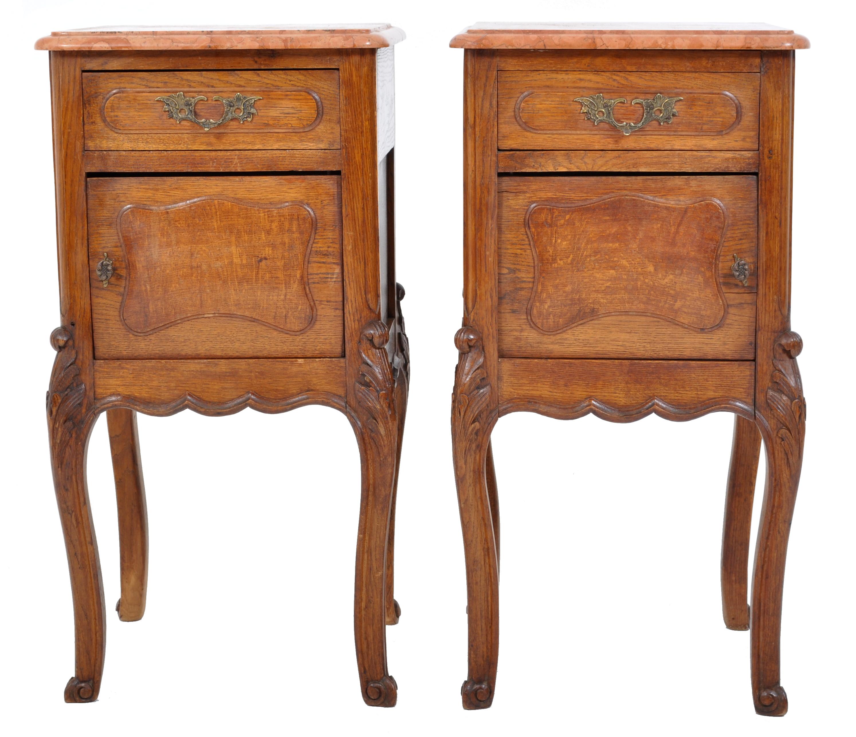 Pair of antique French Provincial carved oak marble top nightstands, circa 1890. The nightstands having variegated salmon colored marble tops, each stand having a single drawer with gilded bronze handles and a panel covered door below. The stands