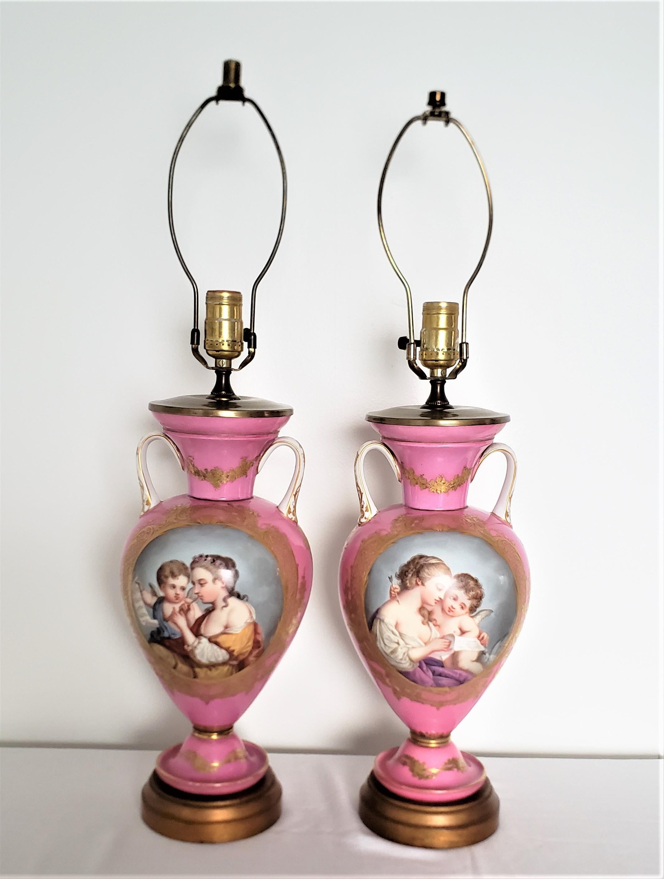 This pair of hand-painted porcelain table lamps are unsigned, but presumed to have originated from France and dating to approximately 1880 and done in a Sevres style. The table lamps have a vivid pink ground with hand painted panels of a young woman