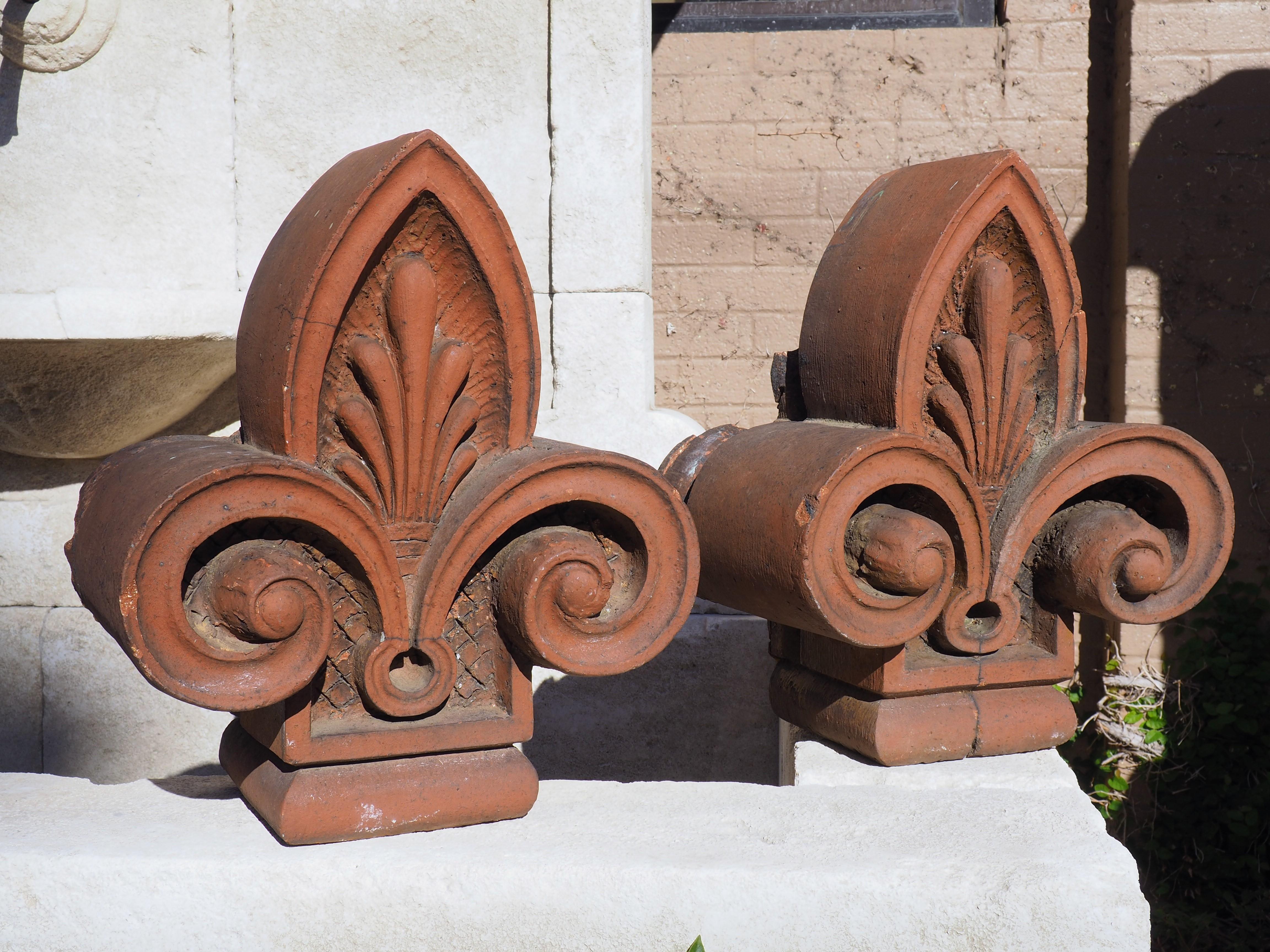 Originally attached to a French building, this pair of terra cotta fleur de lys finials is from circa 1880. The finials still retain their original terra cotta orange color but have developed a dark gray patina from years of exposure to the