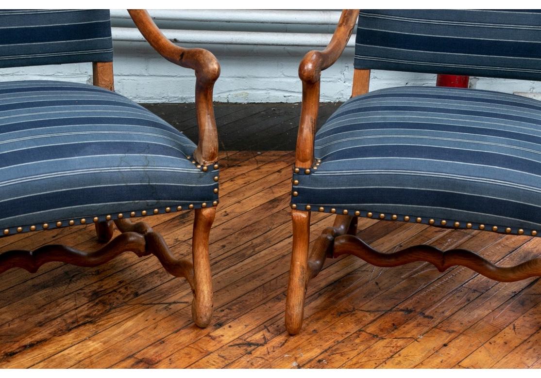A noteworthy pair of large scale antique French carver chairs with fine traditional Rustic form and very good stability, circa 1870. Carved elm with curved arms and legs and having scrolled feet and serpentine H stretchers. In a blue striped fabric