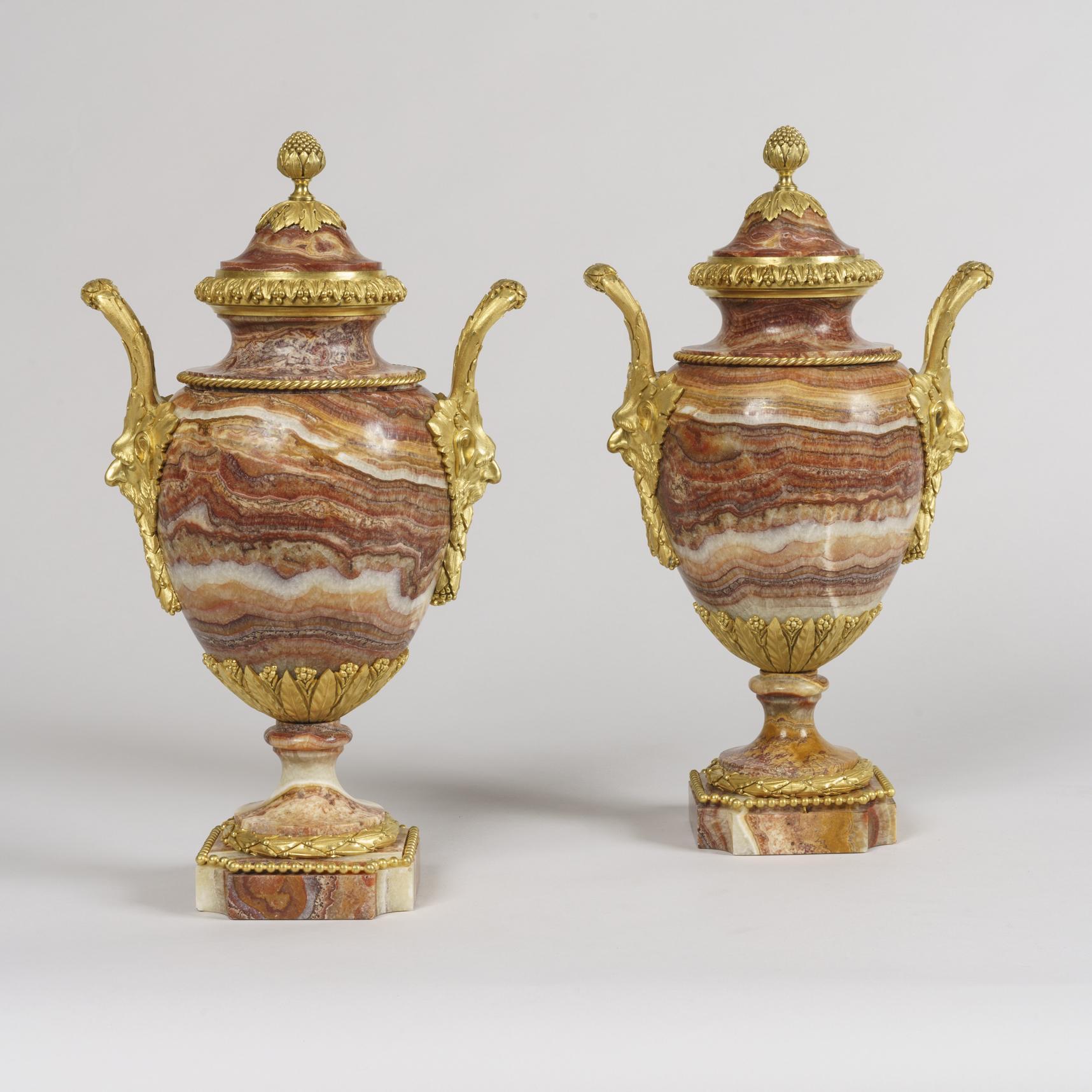 A fine pair of urns in the Louis XVI Manner.

Carved from Egyptian Alabaster Rosso and dressed with gilt-bronze mounts, rising from in-curved square stepped bases, the twin-handled ovoid bodies supported by waisted socles and flanked by bearded