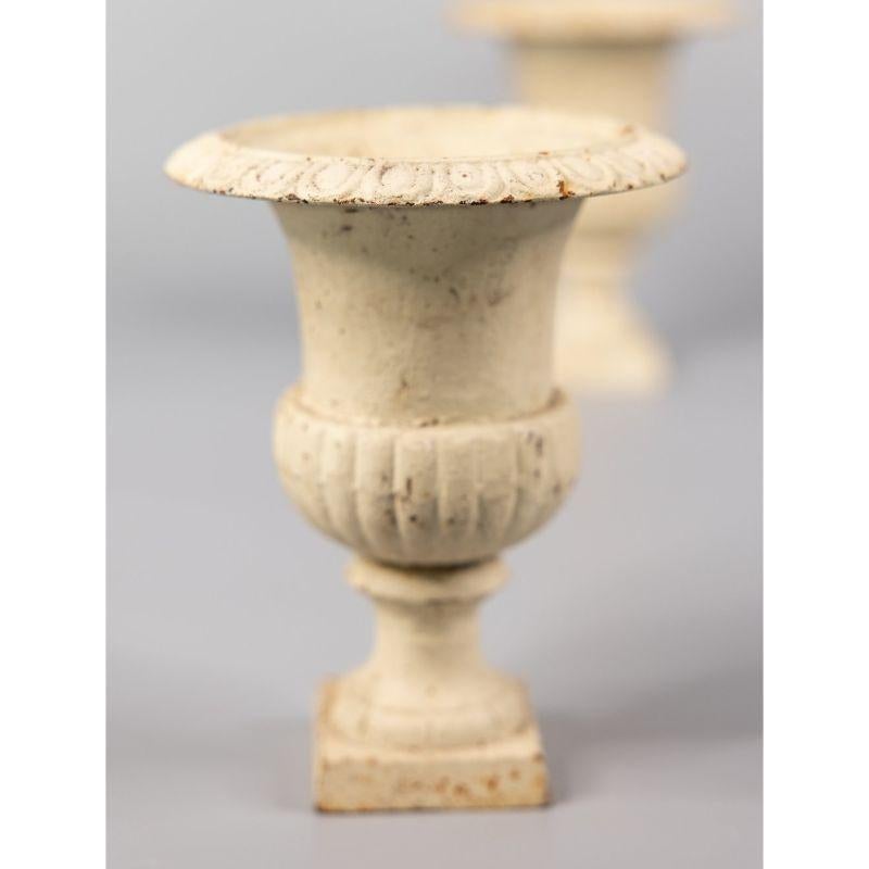 A charming petite pair of antique French Neoclassical style white cast iron urns or planters. These fine urns are solid and heavy with the lovely original patina, and would be fabulous displayed indoors or outdoors.

