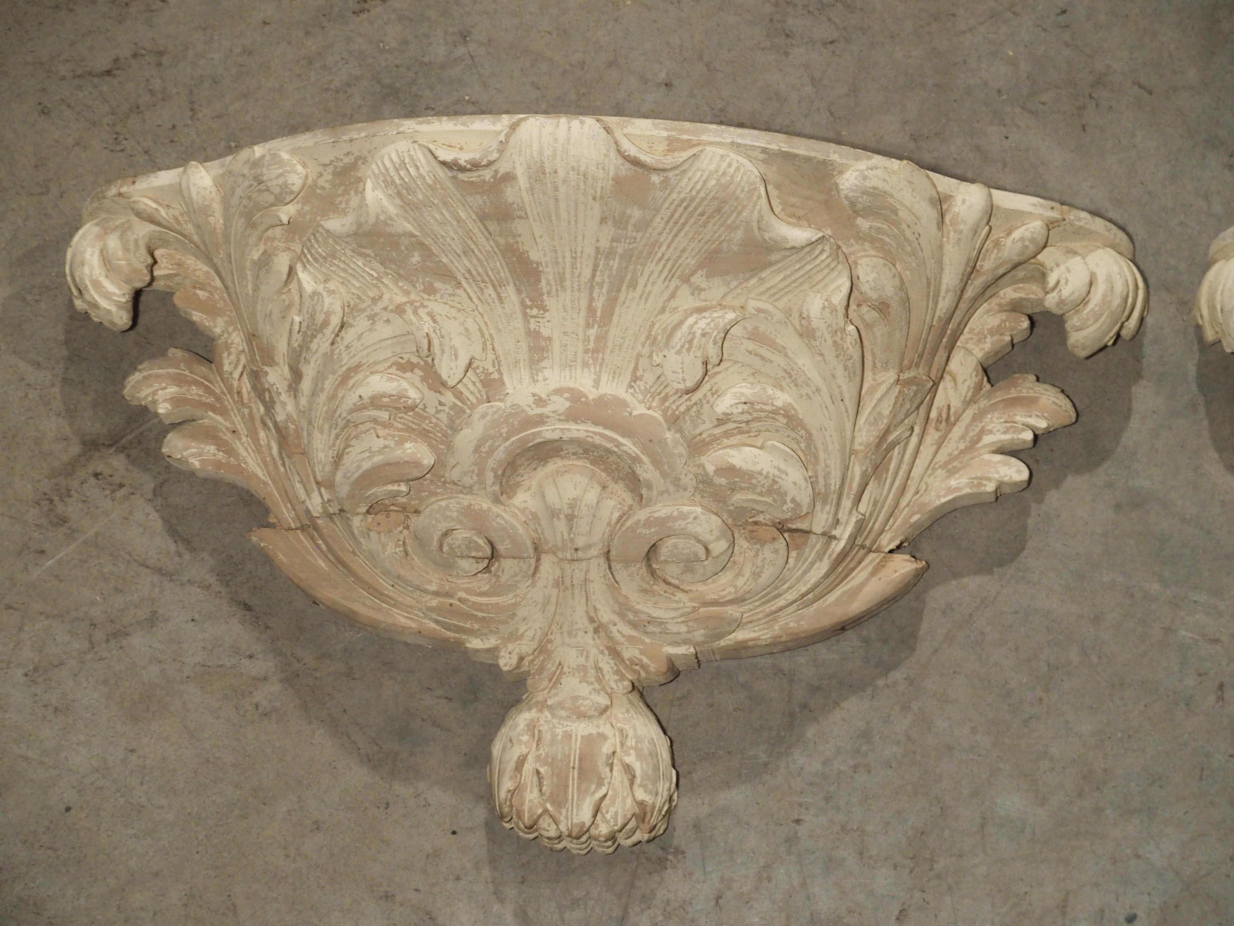 This antique pair of French parcel paint wooden wall brackets are in the forms of half urns. The ornamentation is a stylized shell flanked by graceful scrolling acanthus leaves emanating from a base of foliate C-scrolls with a drop of oak leaves.