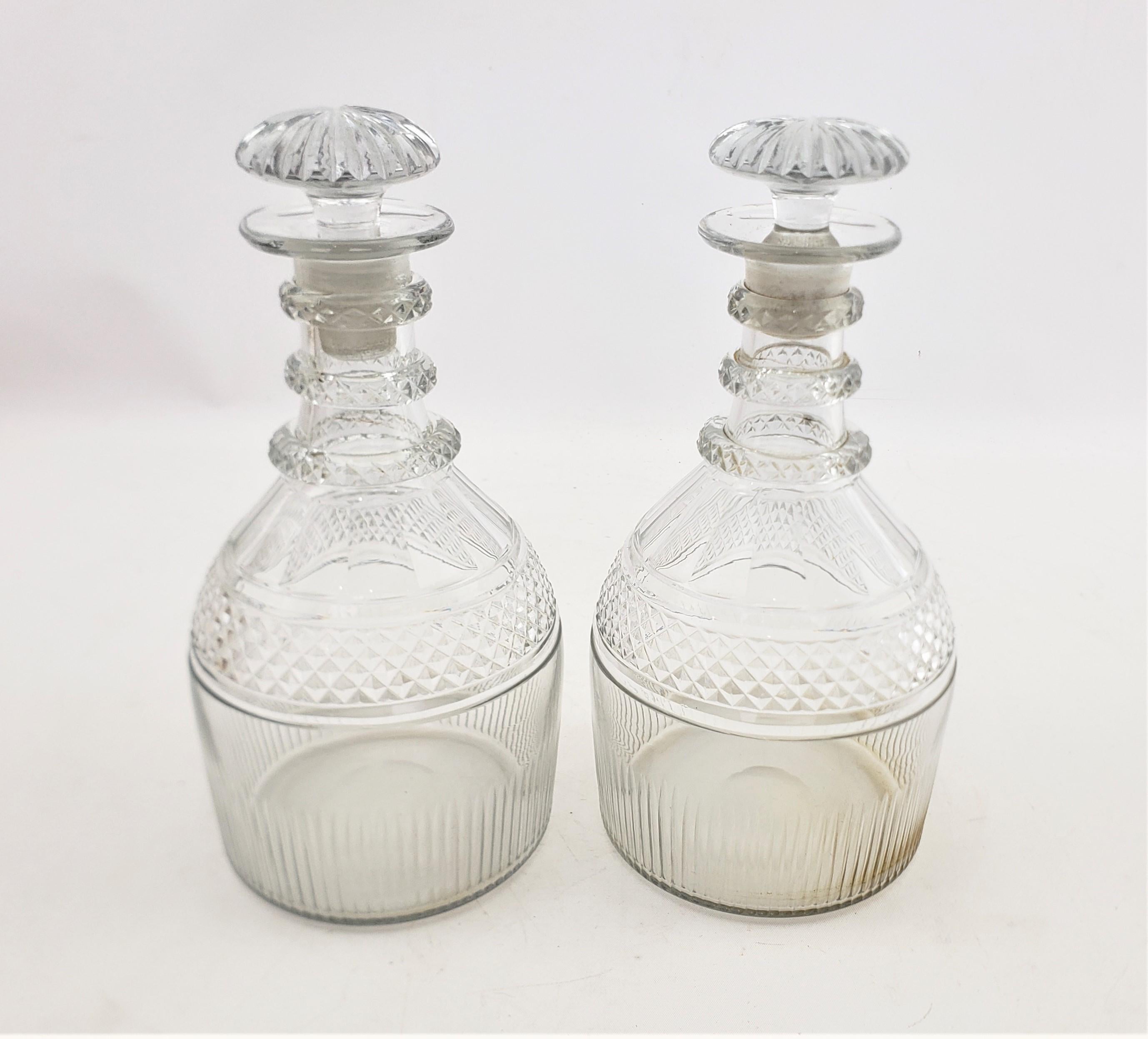 This pair of antique decanters are unsigned, but presumed to have originated from England and date to approximately 1825 and done in a period George III style. The decanters are done in clear glass with faceted mushroom stoppers and a three neck