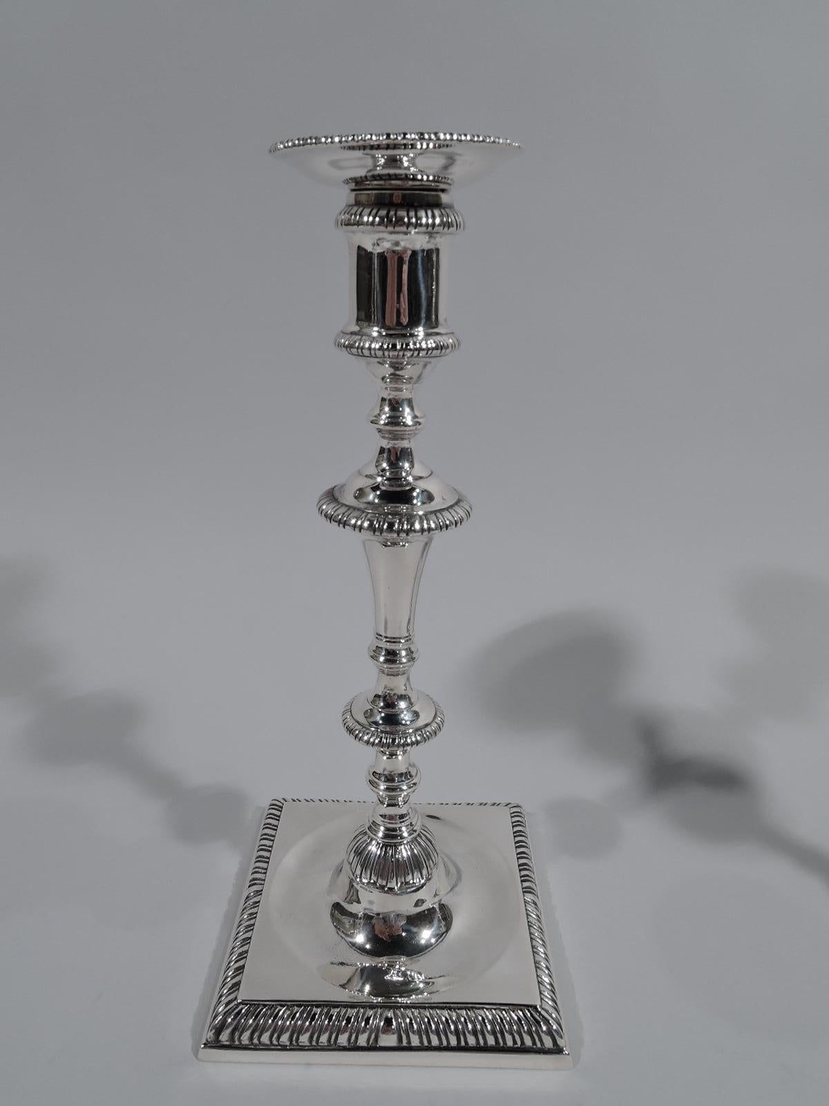 Pair of Georgian-style sterling silver candlesticks. Made by Crichton & Co. Ltd in New York, circa 1920. Each: Spool socket with detachable bobeche on shaft with knops and flanges terminating in leafy-dome on square base. Traditional form with