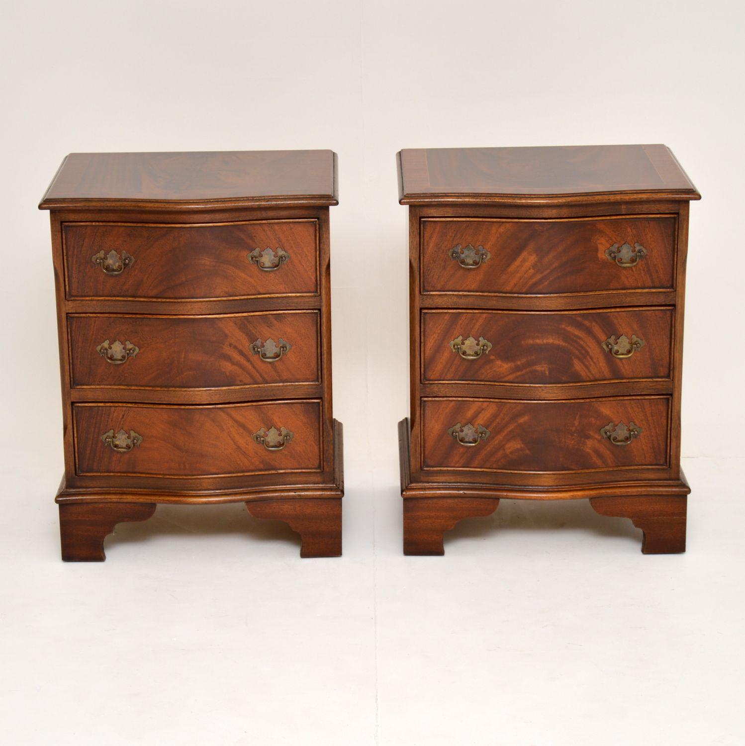 Pair of antique Georgian style flame mahogany bedside chests with serpentine shaped fronts, in excellent condition and dating from the 1950s period.

They have flame mahogany tops with satinwood inlay and mahogany cross banding. There are three