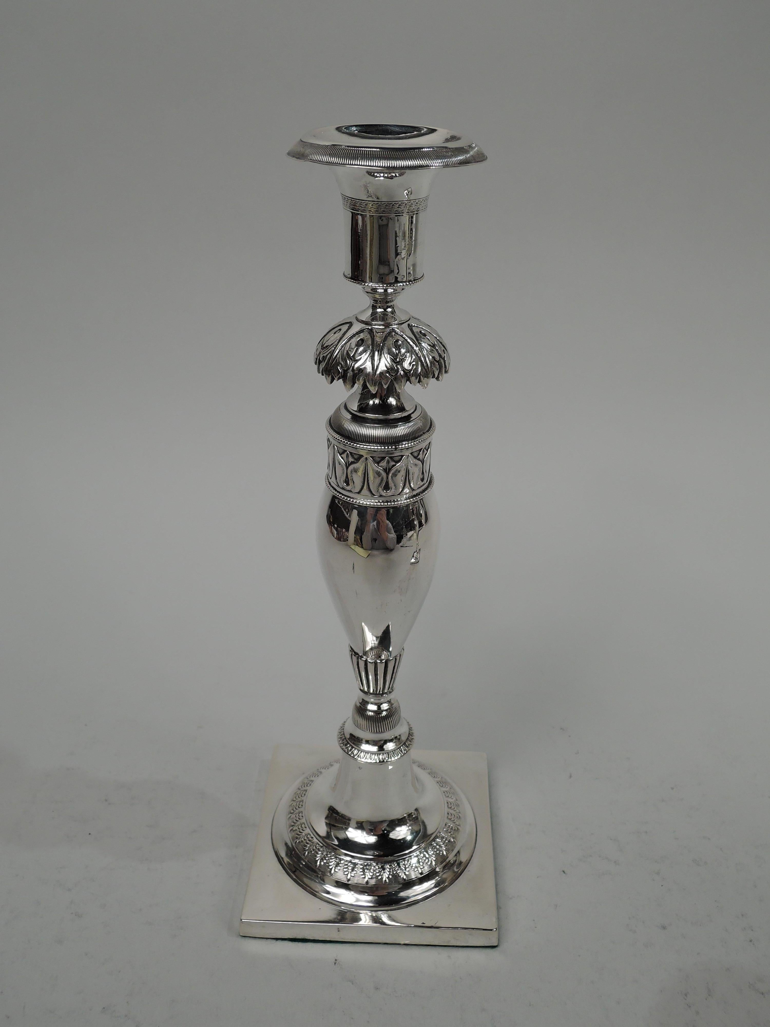 Pair of German Biedermeier Classical silver candlesticks, circa 1830. Each: Socket mounted to leaf flange in turn mounted to baluster shaft on raised round foot on square base. Fluting, gadrooning, acanthus leaf, and leaf-and-dart ornament. Marked.