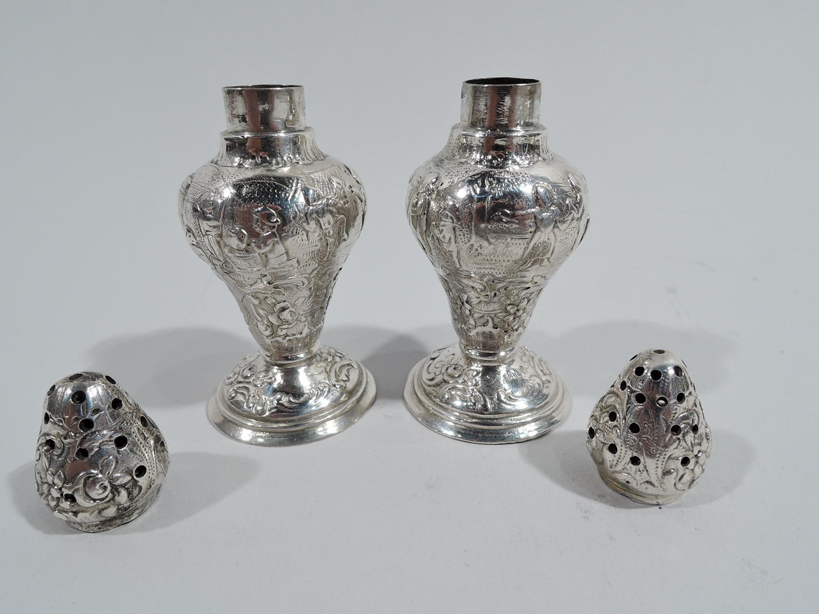 Pair of German 800 silver salt and pepper shakers, ca 1910. Each: Baluster on stepped and domed foot. Pierced ovoid cover. Chased ornament depicting rustic revels with jiggers and topers. Marked. Total weight: 1.7 troy ounces.