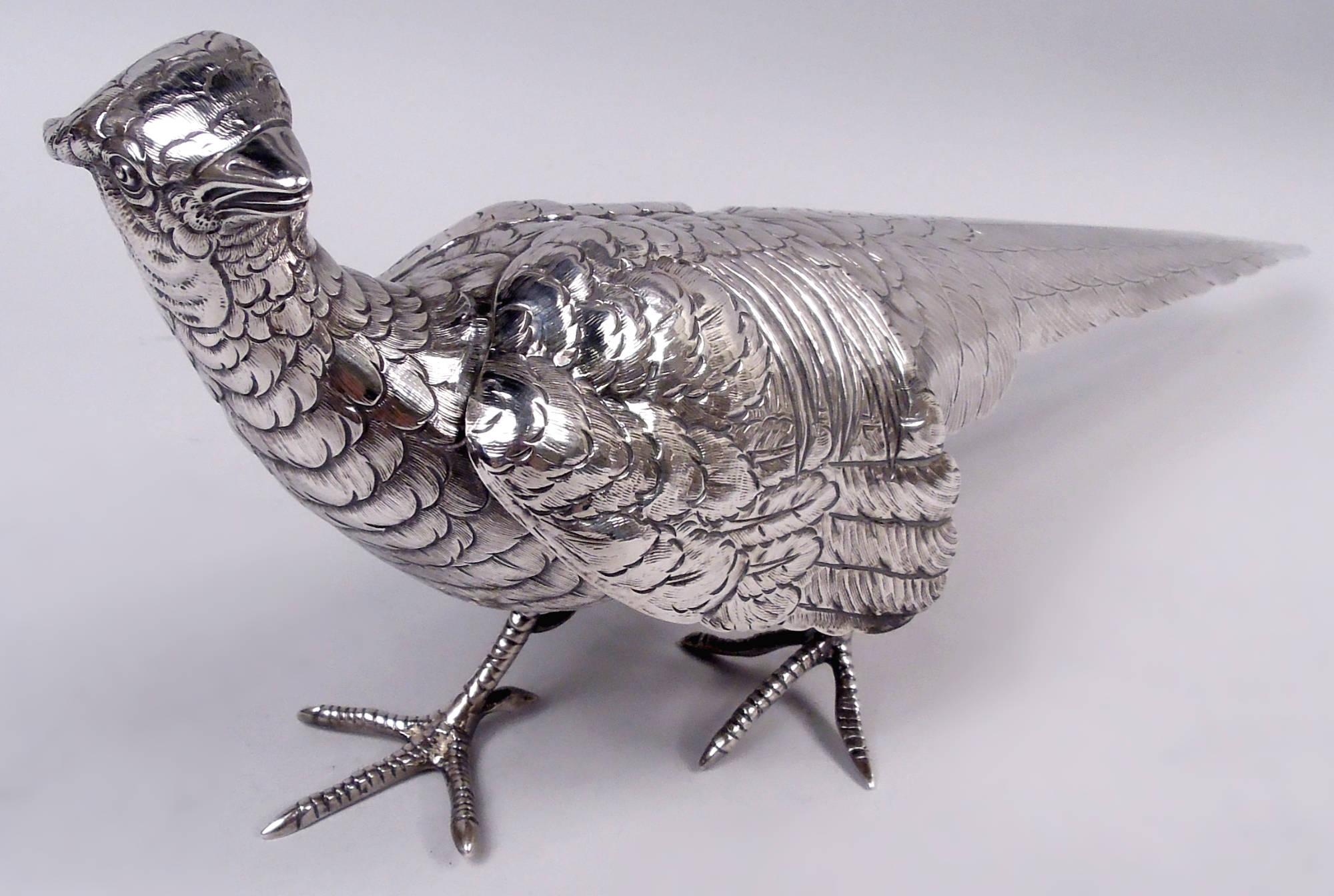 Paire de faisans en argent allemand, vers 1920. Les oiseaux sont attrapés à mi-chemin par des serres écailleuses. Le coq a les ailes repliées et regarde avec méfiance sur le côté tandis que la poule bat nerveusement des ailes. Un couple séduisant