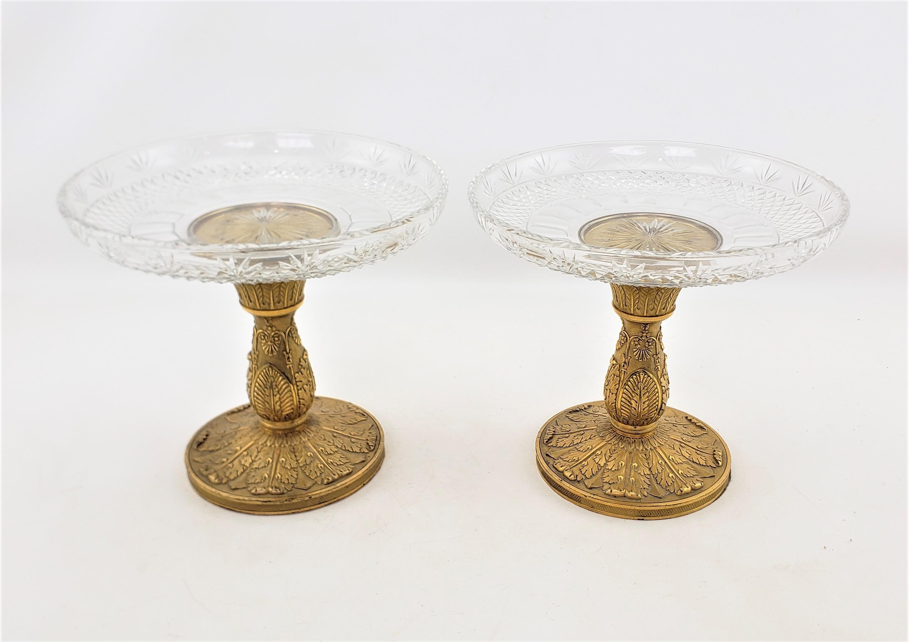 This pair of antique tazzas are unsigned, but presumed to have originated from France and date to approximately 1900 and done in a Neoclassical style. The tops are done in a clear cut crystal with a cross pattern and the bases are done in a cast