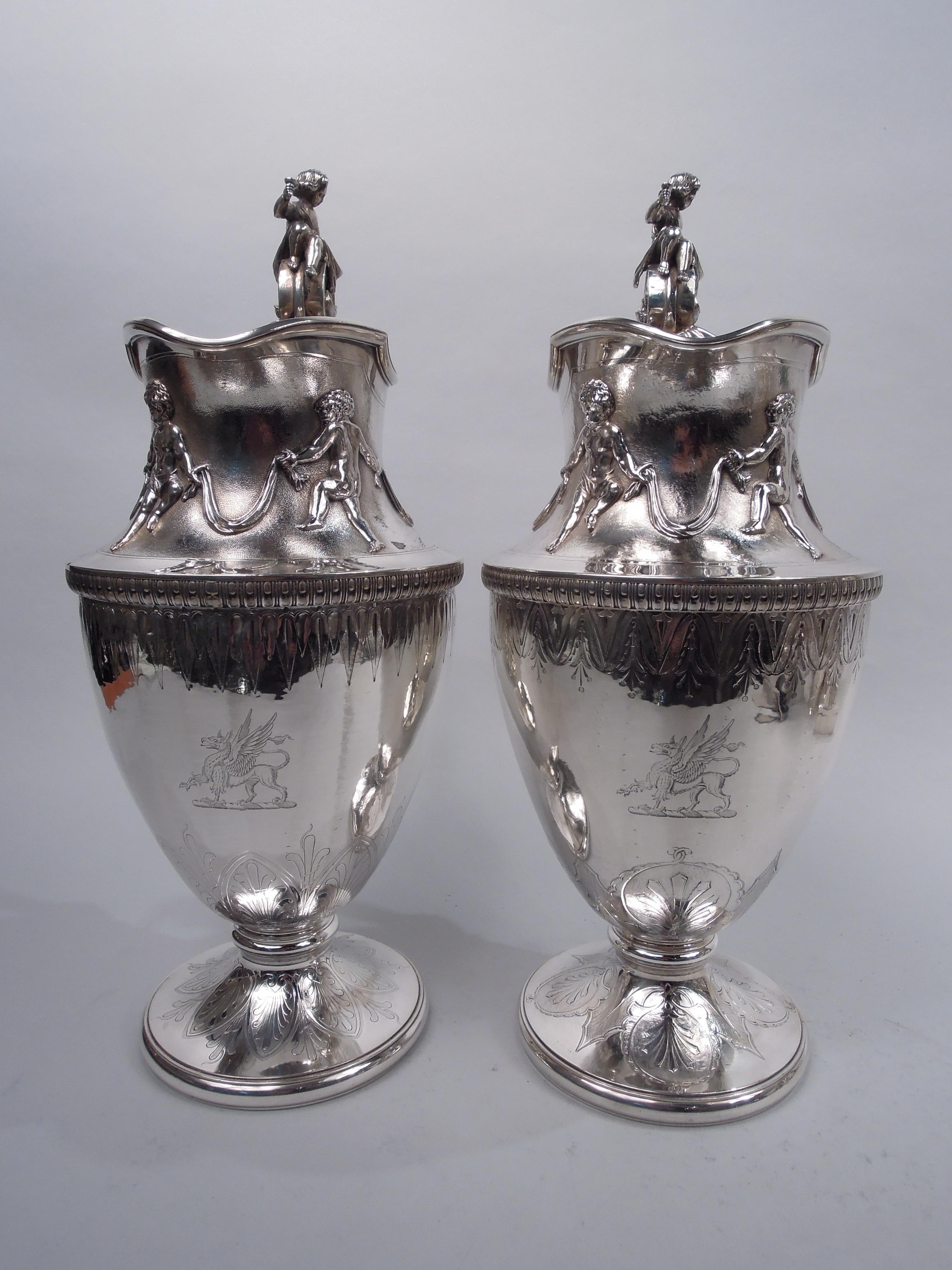 Pair of striking midcentury Classical coin silver ewers. Made by Gorham in Providence, ca 1860. Each: Ovoid bowl with helmet mouth and raised foot. On neck applied frieze with ring of Bacchic boys gripping drapery swags; below applied bead-and-reel