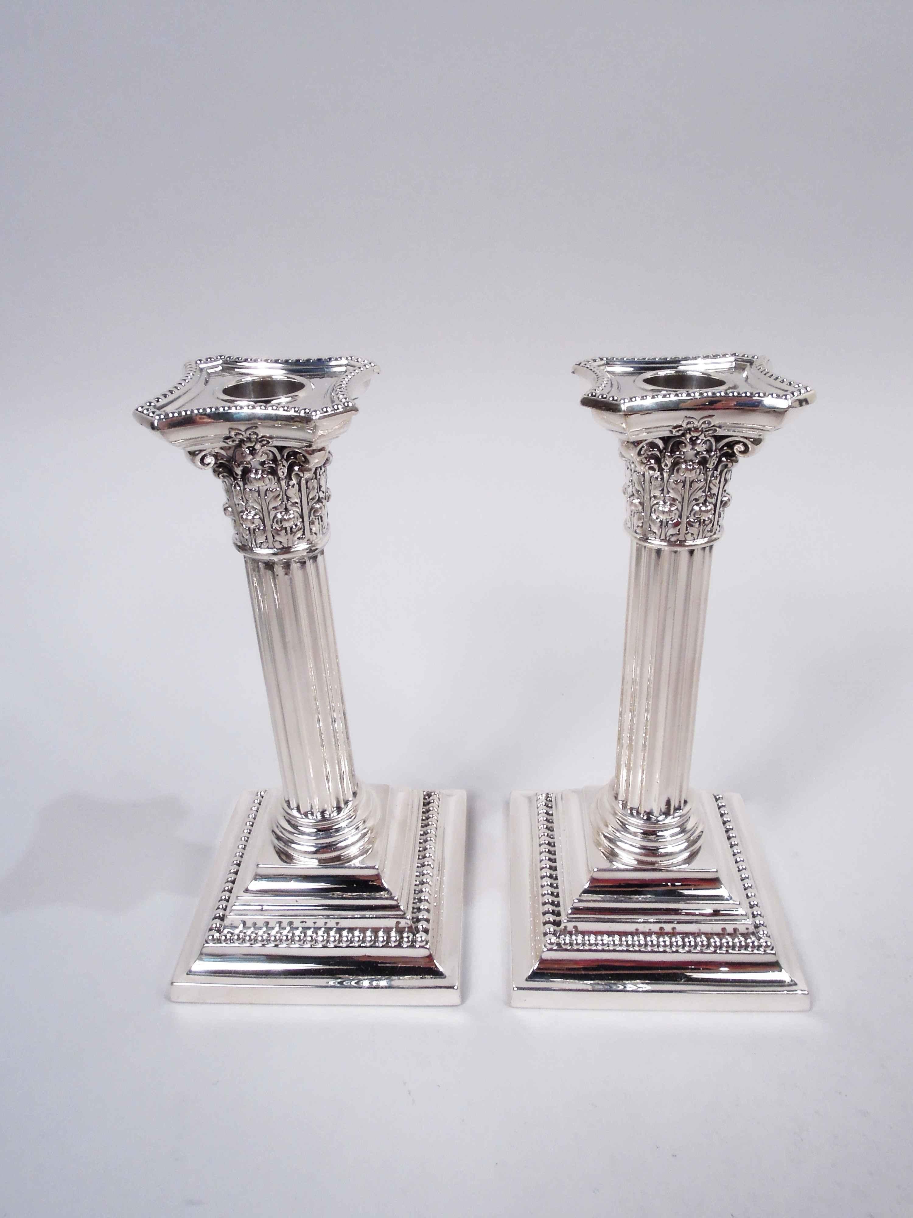 Pair of Edwardian Classical sterling silver column candlesticks. Made by Gorham in Providence, ca 1910. Each: Column with fluted shaft on stepped square base. Corinthian capital with chamfered and concave bobeche. Beading. Fully marked including