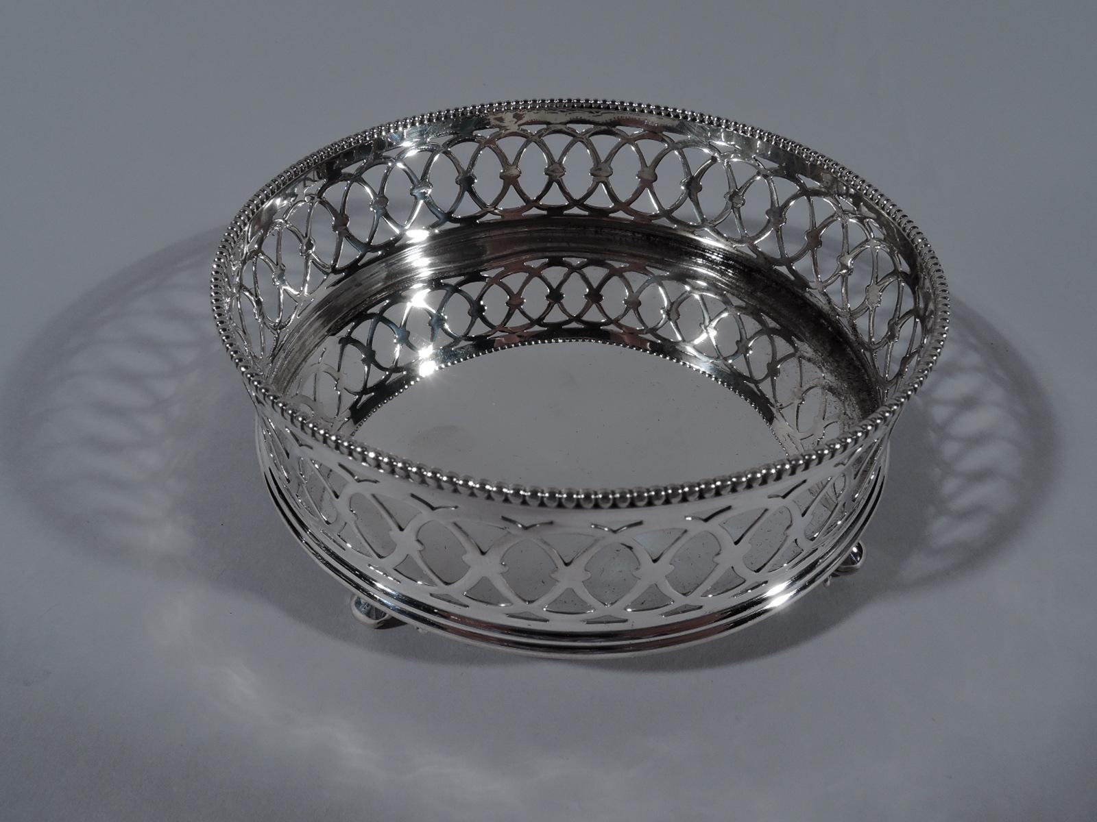Pair of Edwardian sterling silver wine bottle coasters. Made by Gorham in Providence in 1896. Each: Round with gallery sides comprising pierced interlaced circles, and beaded rim. Four leaf-mounted volute supports. Fully marked including date symbol
