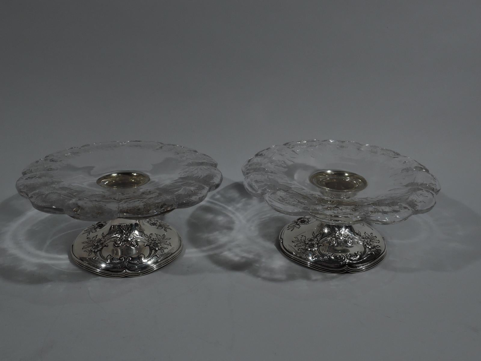 Pair of Edwardian sterling silver and crystal compotes. Made by Gorham in Providence, circa 1910. Each: Shallow clear crystal bowl with etched flowers and gently turned-down scalloped rim mounted to raised foot with chased flowers and reeded and