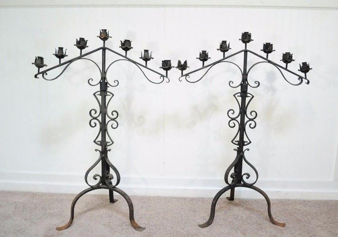 Pair of tall and stately antique Gothic/Mission Revival adjustable height wrought iron candelabras. Item features seven candleholders each, scrolling wrought iron forms, adjustable height, and Classic Gothic styling as well as a desirable