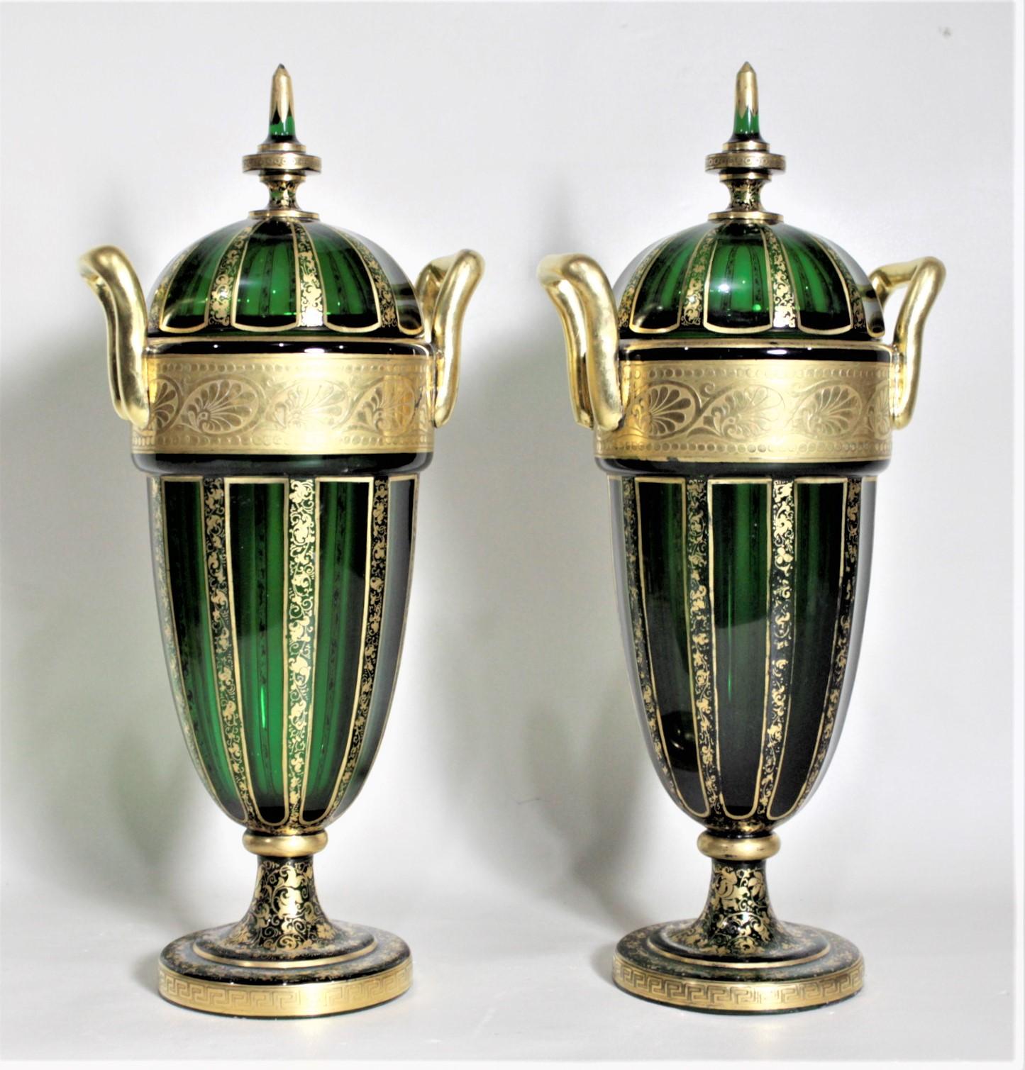 This pair of antique Bohemian glass covered urns or vases were handcrafted in circa 1880 in the period Victorian style. The urns are done in a deep green with intricate gilt decoration in a scrolling leaf done around the upper rim and down the
