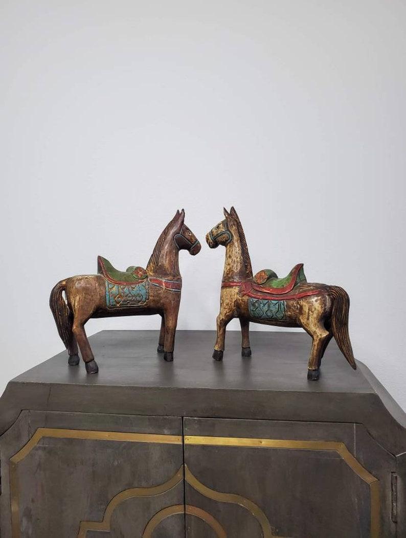 A pair of delightful antique hand carved, sculpted, gessoed, and painted folk art horses. Likely born in India, early 20th century, the similarly styled but not matching pair of unique wooden horse statues display richly detailed carvings and bright