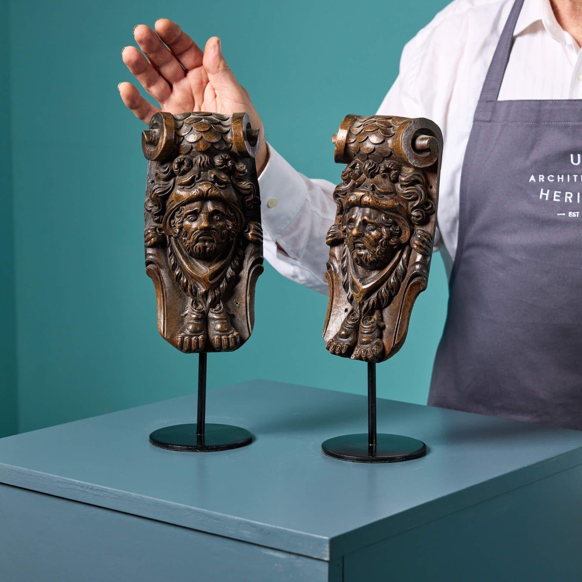 A pair of hand carved English wooden corbels carved in walnut and mounted onto bespoke steel bases for display. Dating from the mid 19th century, these decorative wooden corbels are handsomely carved, depicting masks that seem to peer out of a