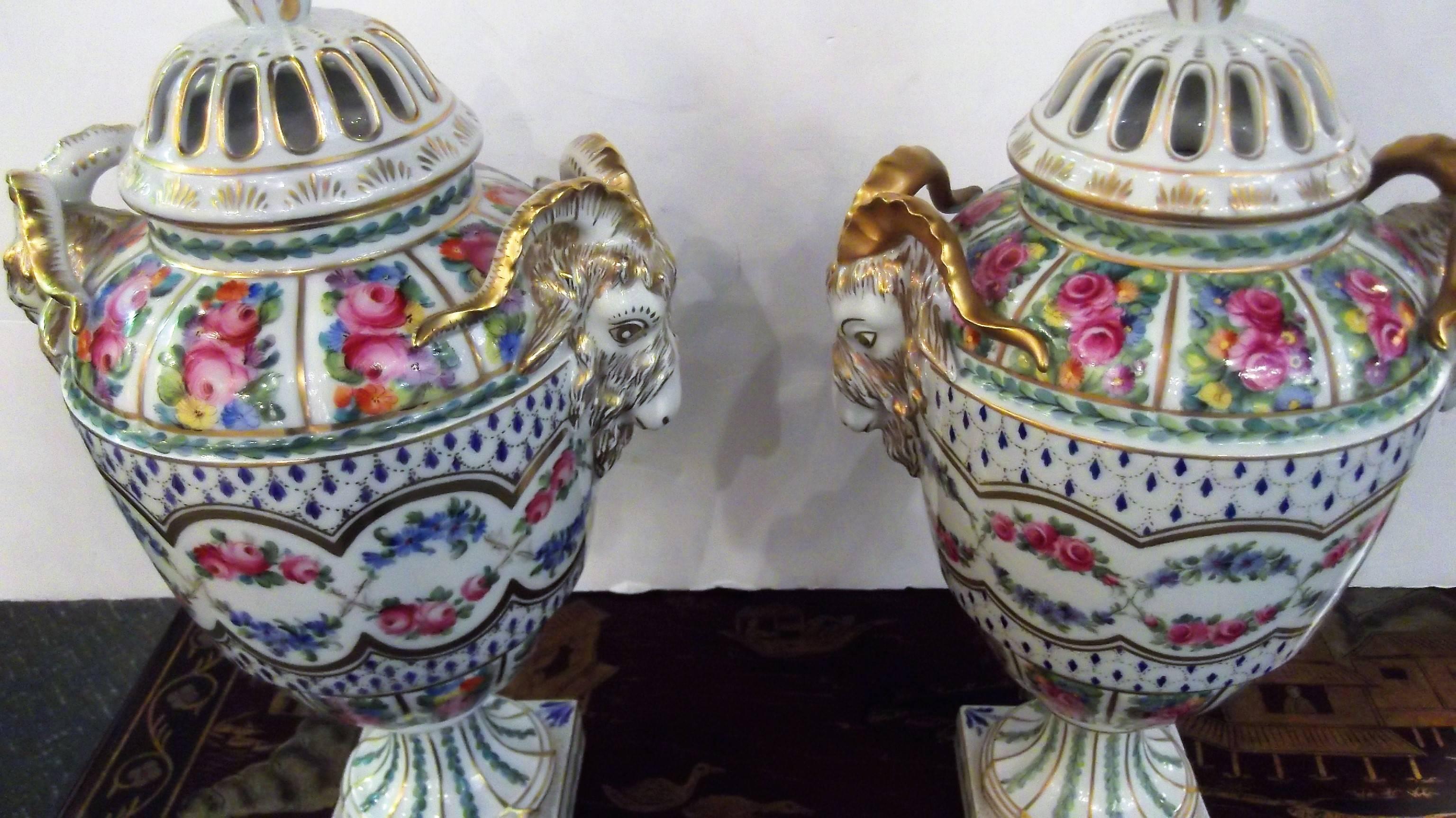 An impressive Dresden hand painted floral and gilt appointed ram's head urn. A gilt final topped on the pierced lid. The body is expertly hand decorated with gilt accents, floral swags and bouquets. All hand painted to perfection.
The urn resting