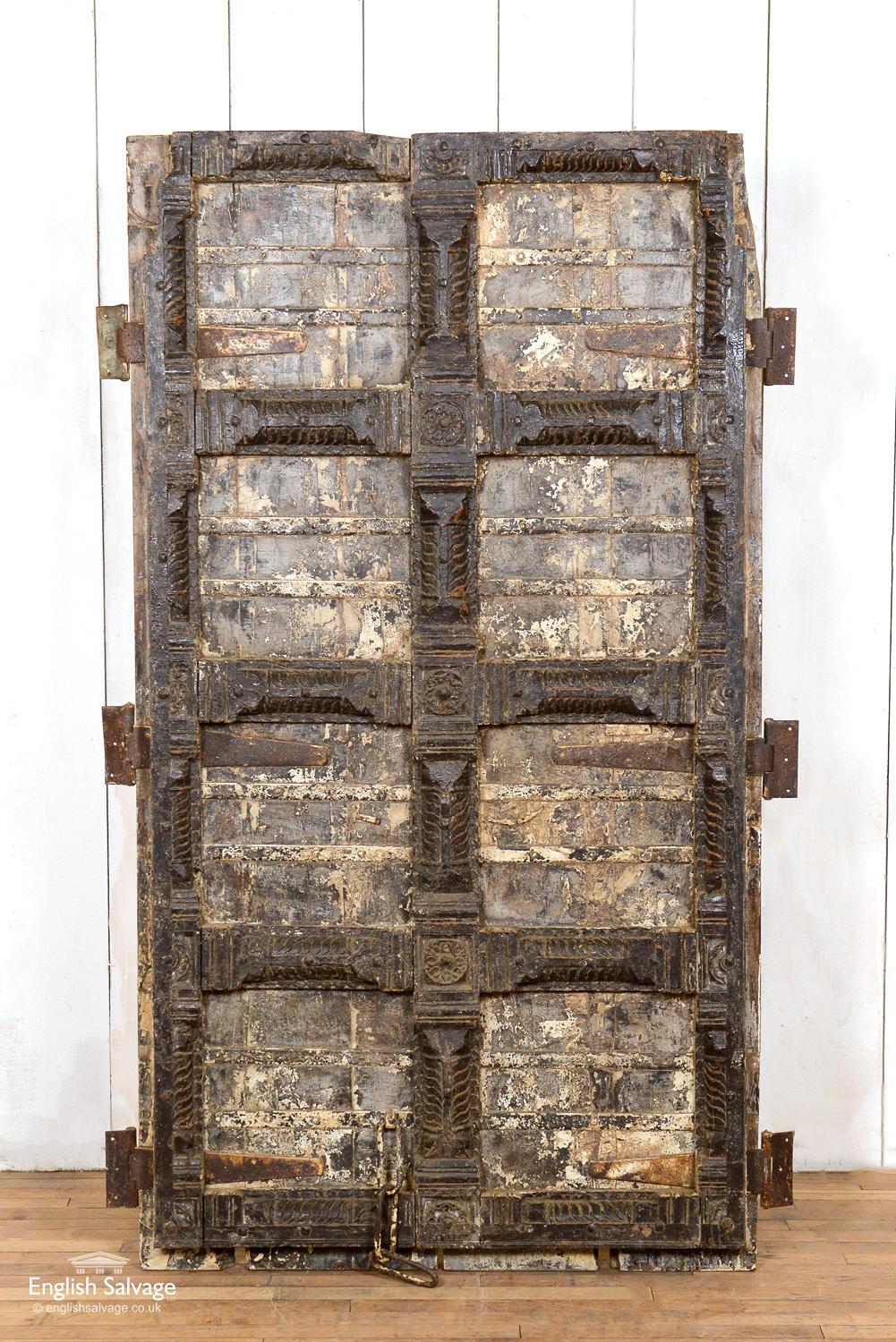 A set of heavy panelled teak doors from Gujarat state in India. Lovely carvings to the door fronts. Very weathered/scuffed paintwork. Reinforced with metal straps. The rear side of the doors are plain with a simple chain lock. There are some splits