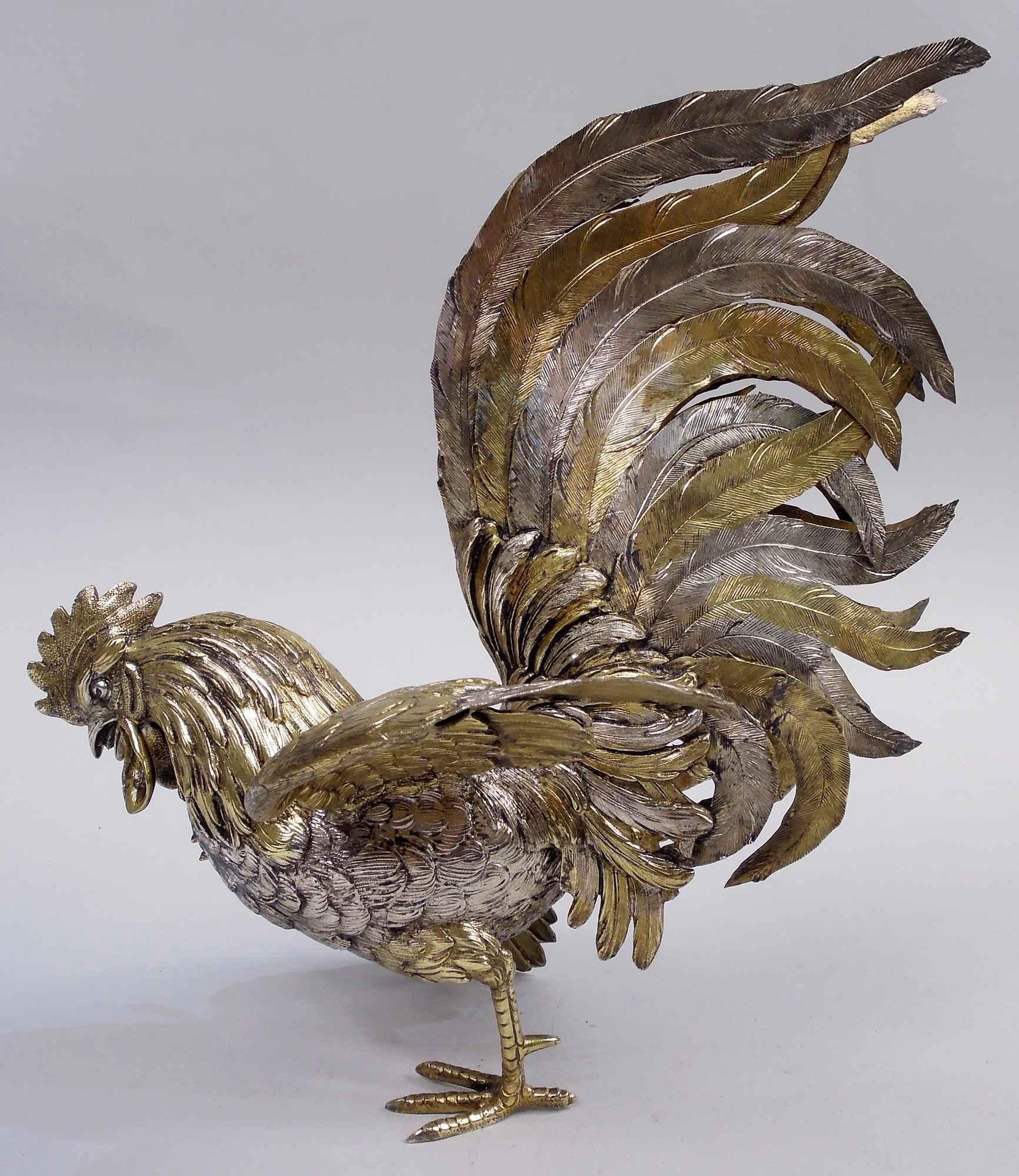 Paire de coqs en argent doré, vers 1930. La tension monte avec les croassements de becs, les battements d'ailes et les serres levées. Le cou hirsute et les plumes de la queue frémissante et flasque. Une bagarre de basse-cour au centre de la table du