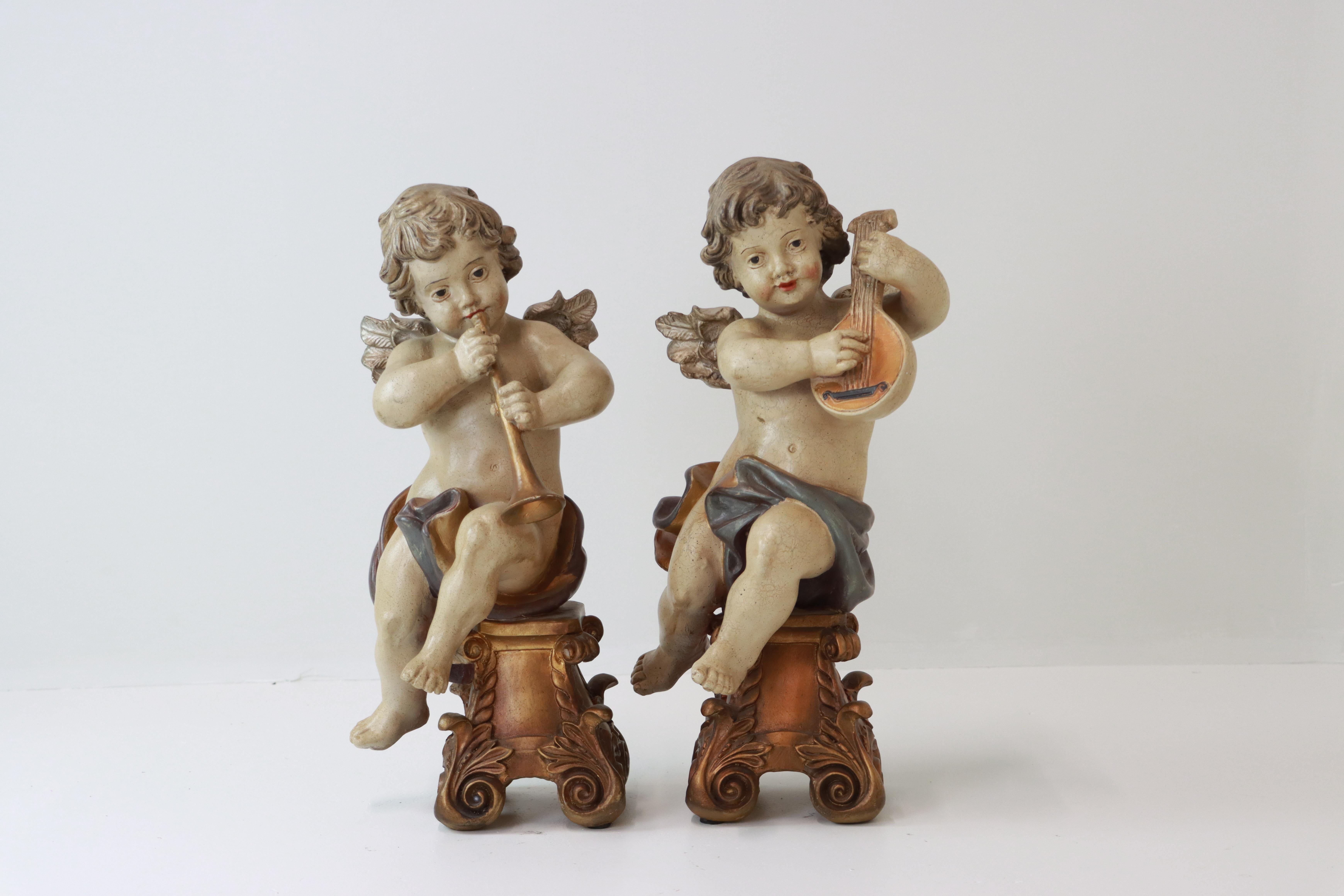 Una bella coppia di putti in legno intagliati e dipinti in policromia in stile barocco. Ogni putto è seduto su una base di piedistallo dorata e a volute. Uno tiene in mano un liuto, l'altro uno shawm, entrambi con tratti dolci e delicati e con ali