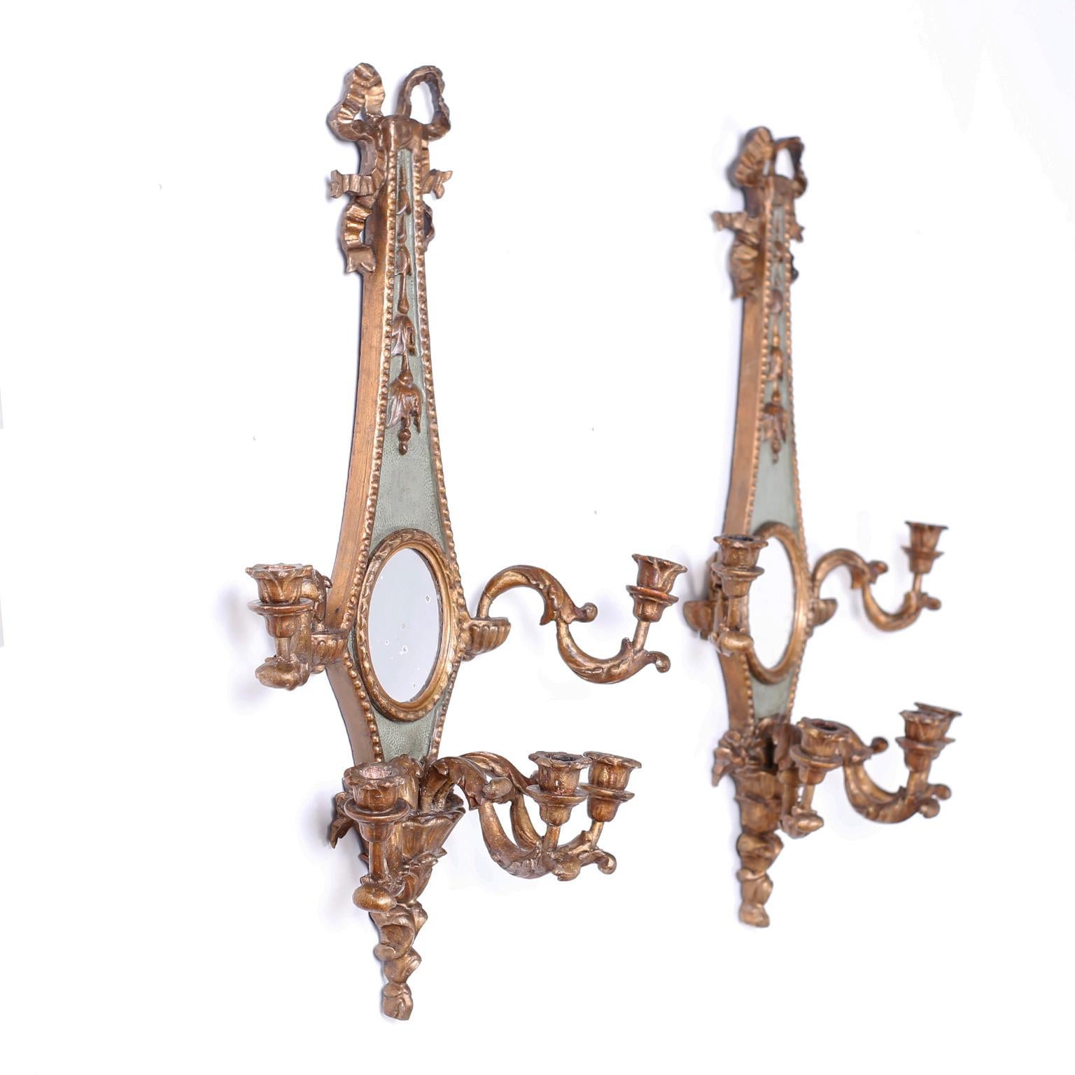 Pair of 19th century Italian five light carved wood wall sconces with a graceful classical form and having distressed oval mirrors on a green painted background. The carved ribbons, flowers and candle stick arms are water gilt with an age acquired